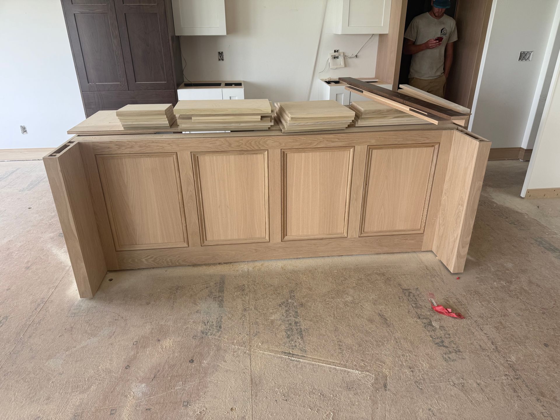 Unfinished oak kitchen island with panel doors, in a room under construction, with a person in the background.