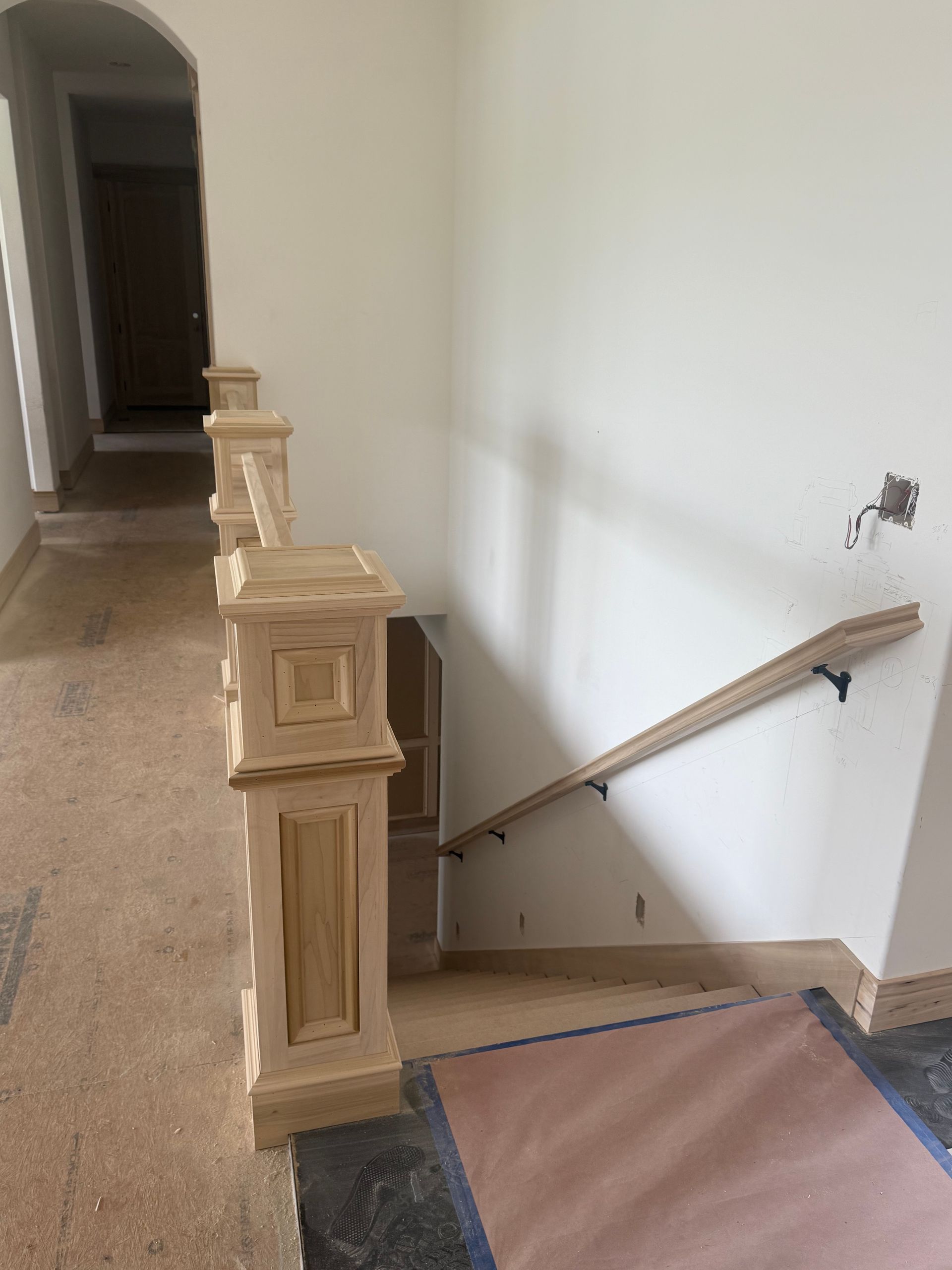 Wooden banister with square posts, and a handrail next to a staircase.