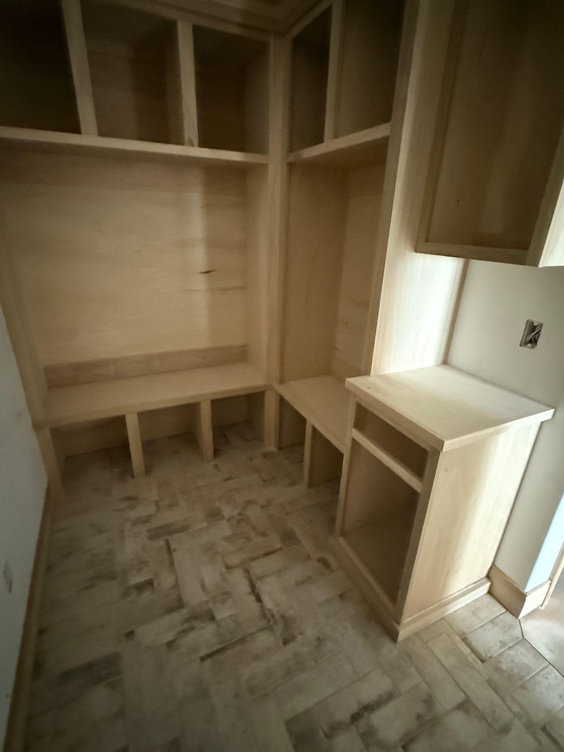 Empty unfinished wooden built-in bench and cabinets. Brown and tan. Tile floor.
