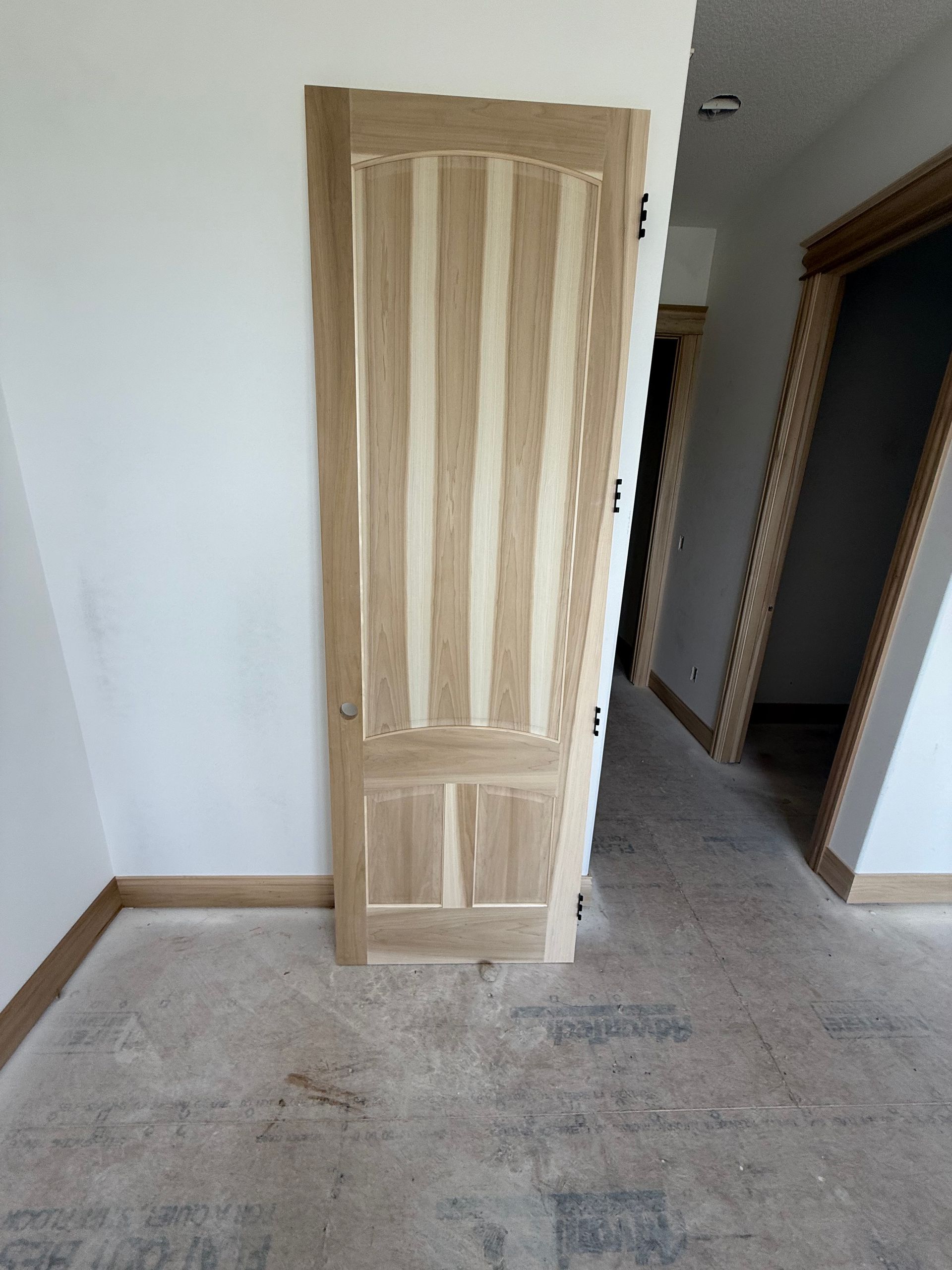 Wooden door, partially open in hallway, next to white wall. Door is light brown.
