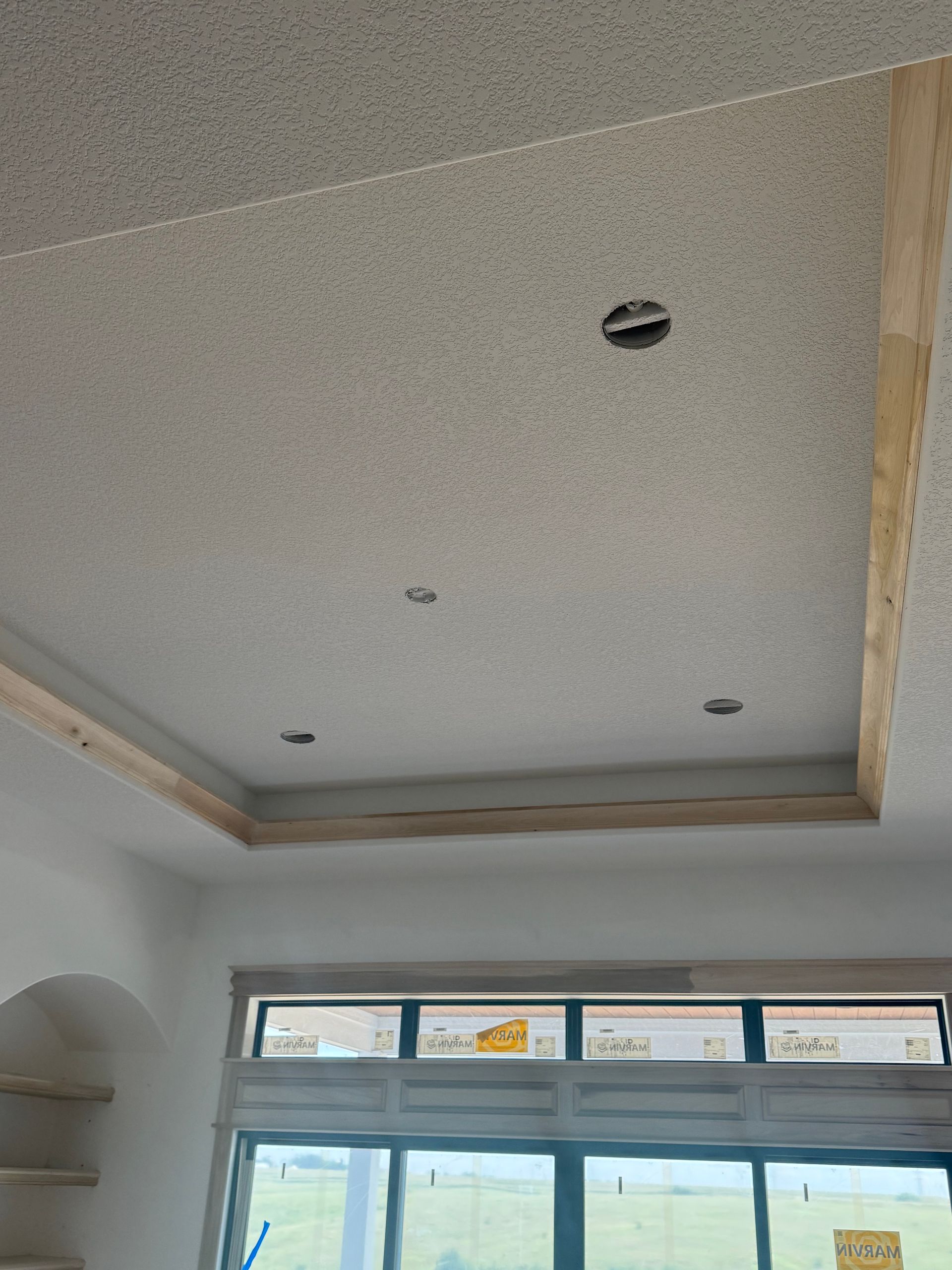 Ceiling with recessed lighting and wooden trim. Textured surface and a window visible below.