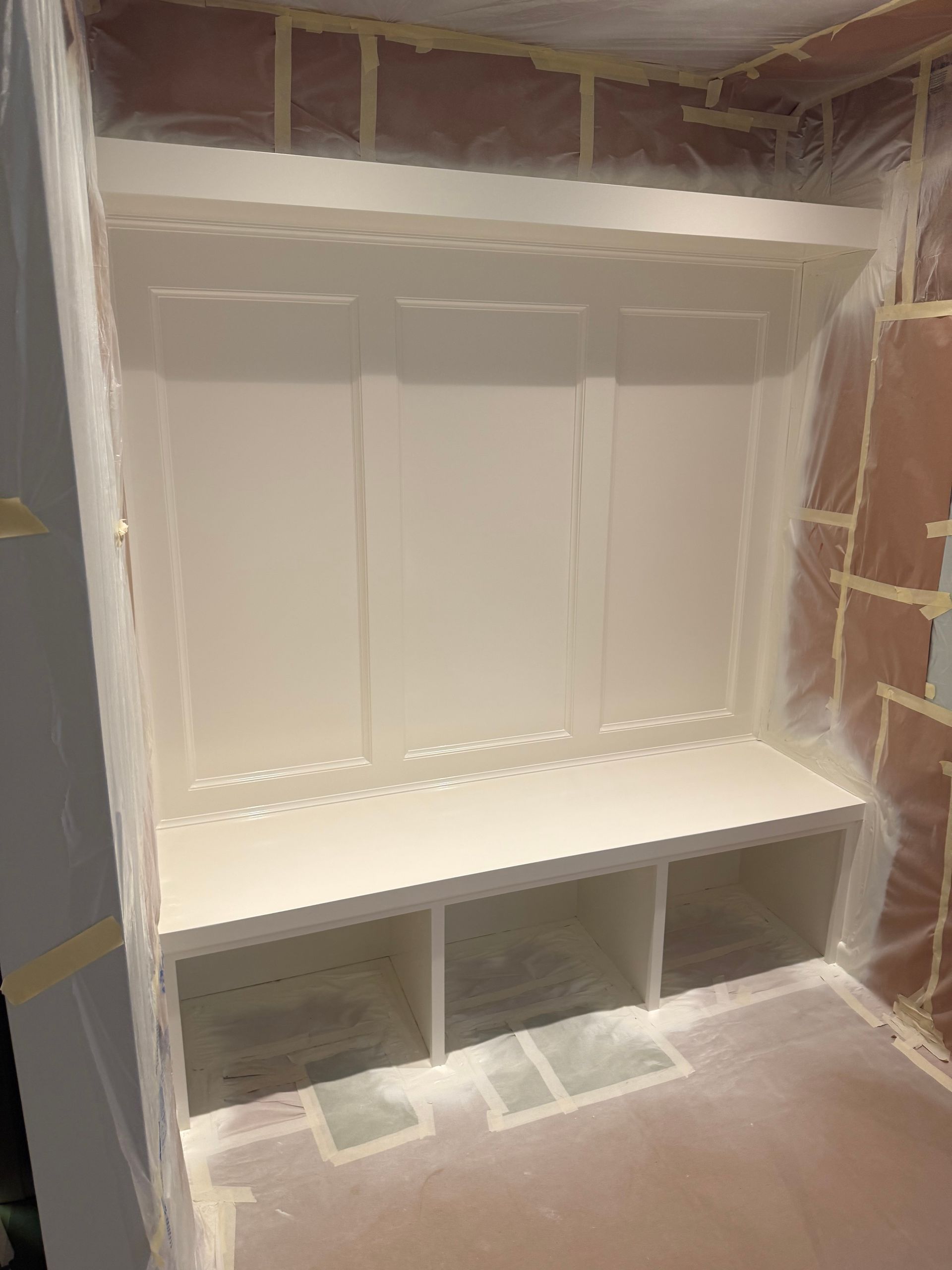 Built-in white storage unit with bench and cubbies being painted in a room.