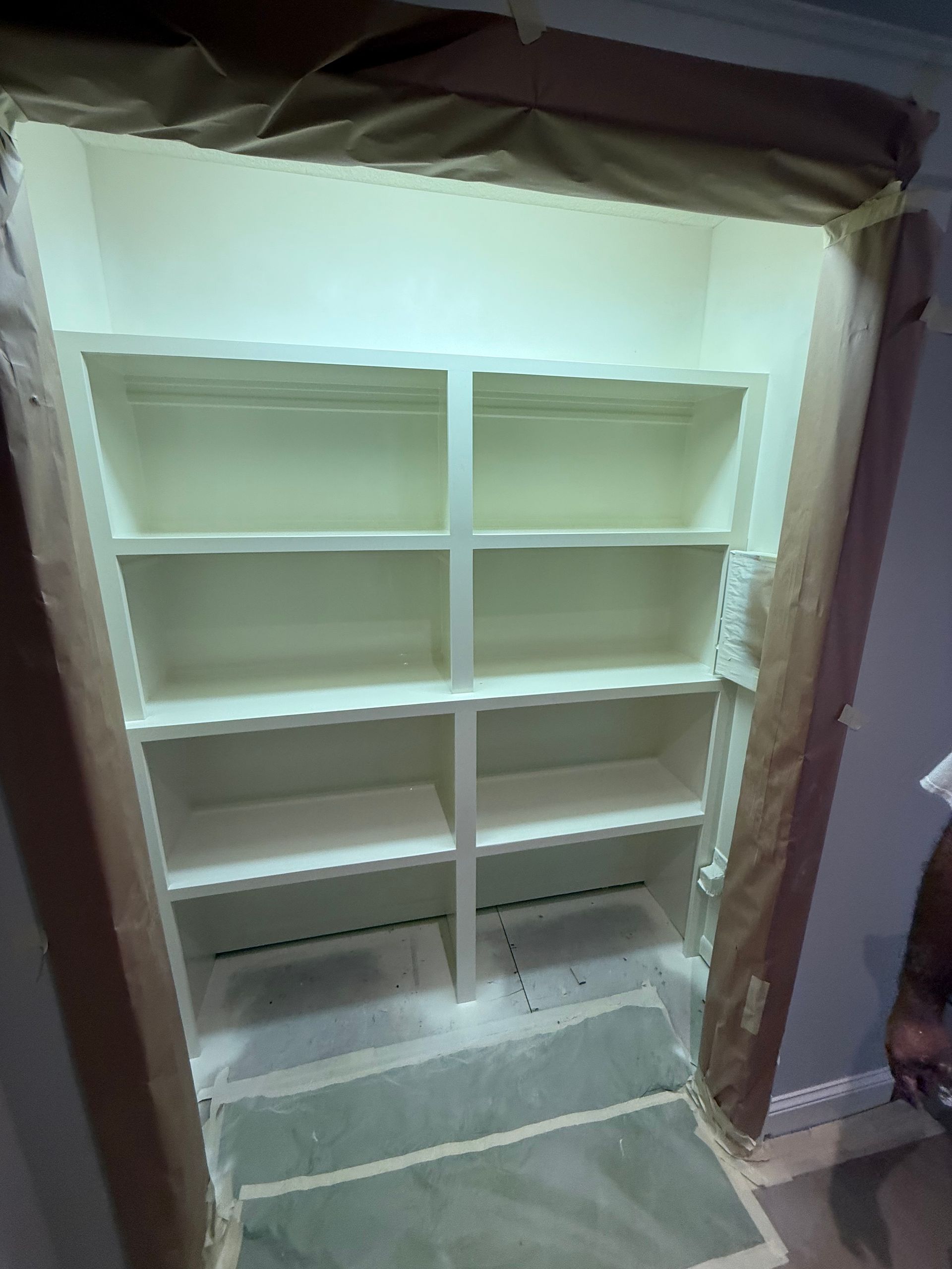 Built-in white shelving unit inside a doorway, masked for painting.