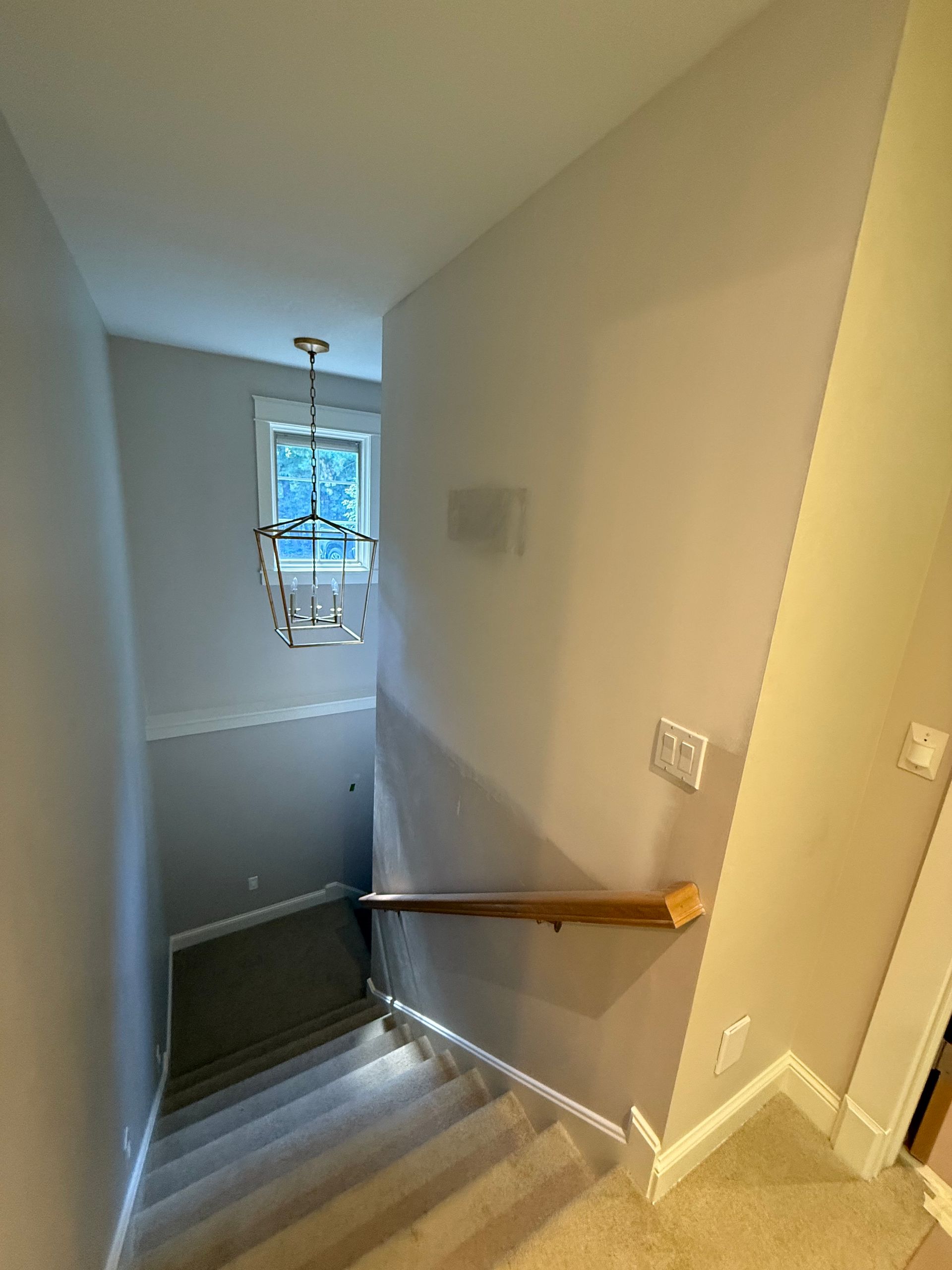 Staircase with light fixture and window at top; beige carpet and walls.