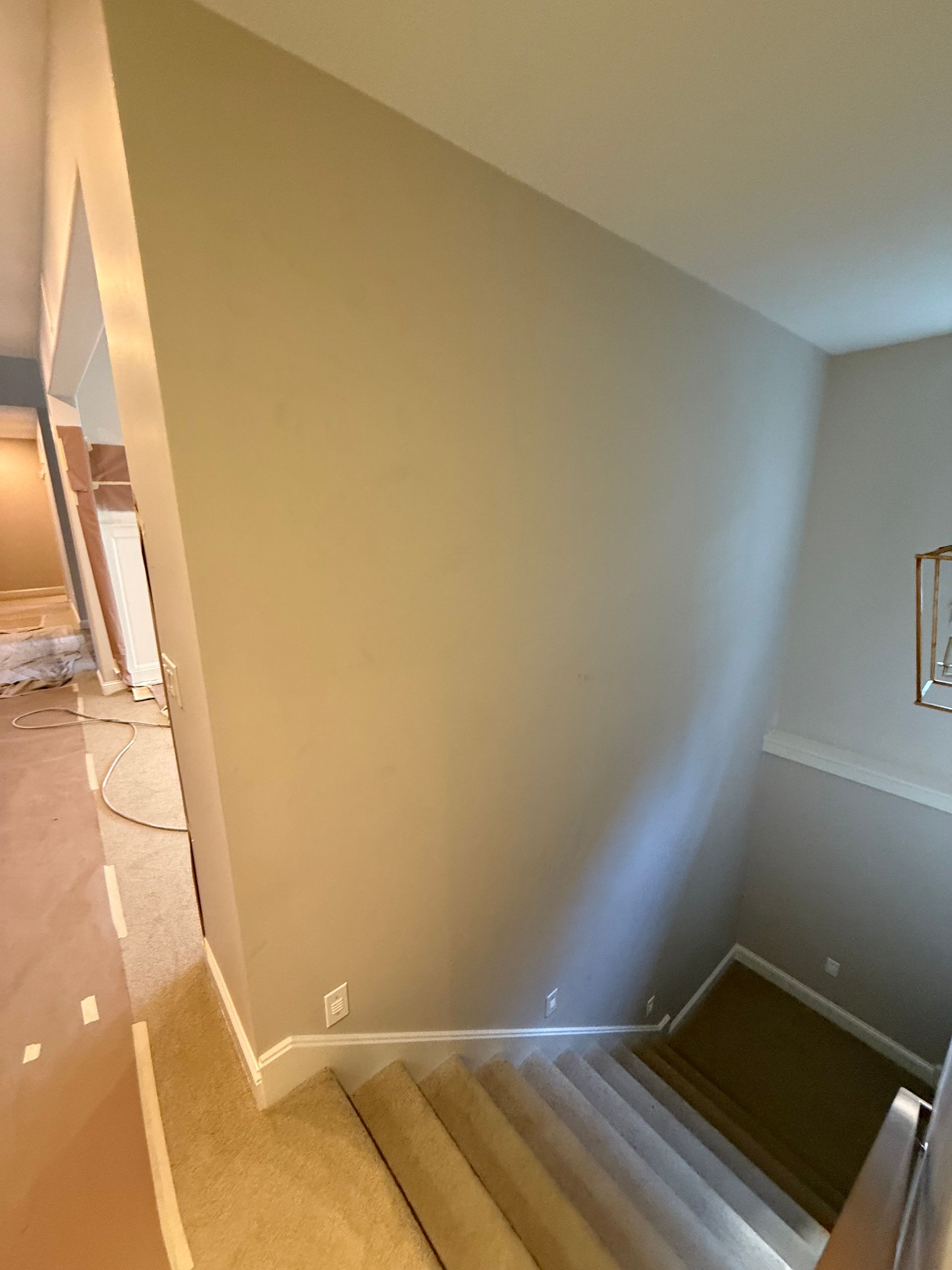 Staircase with beige carpet and walls, leading down. White trim. Open doorway to the left.