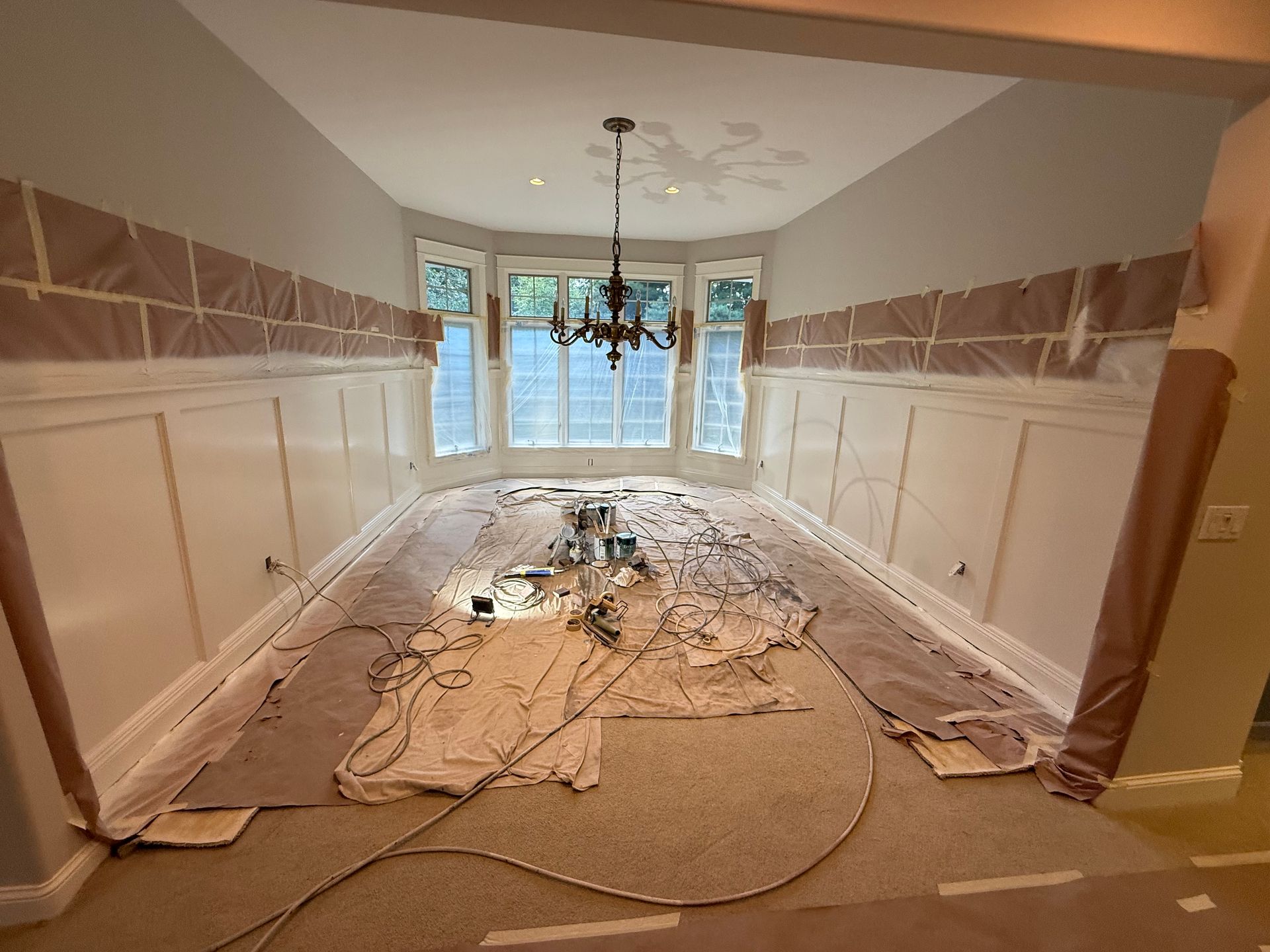 Dining room under renovation, with white wainscoting, beige walls, and protective coverings.
