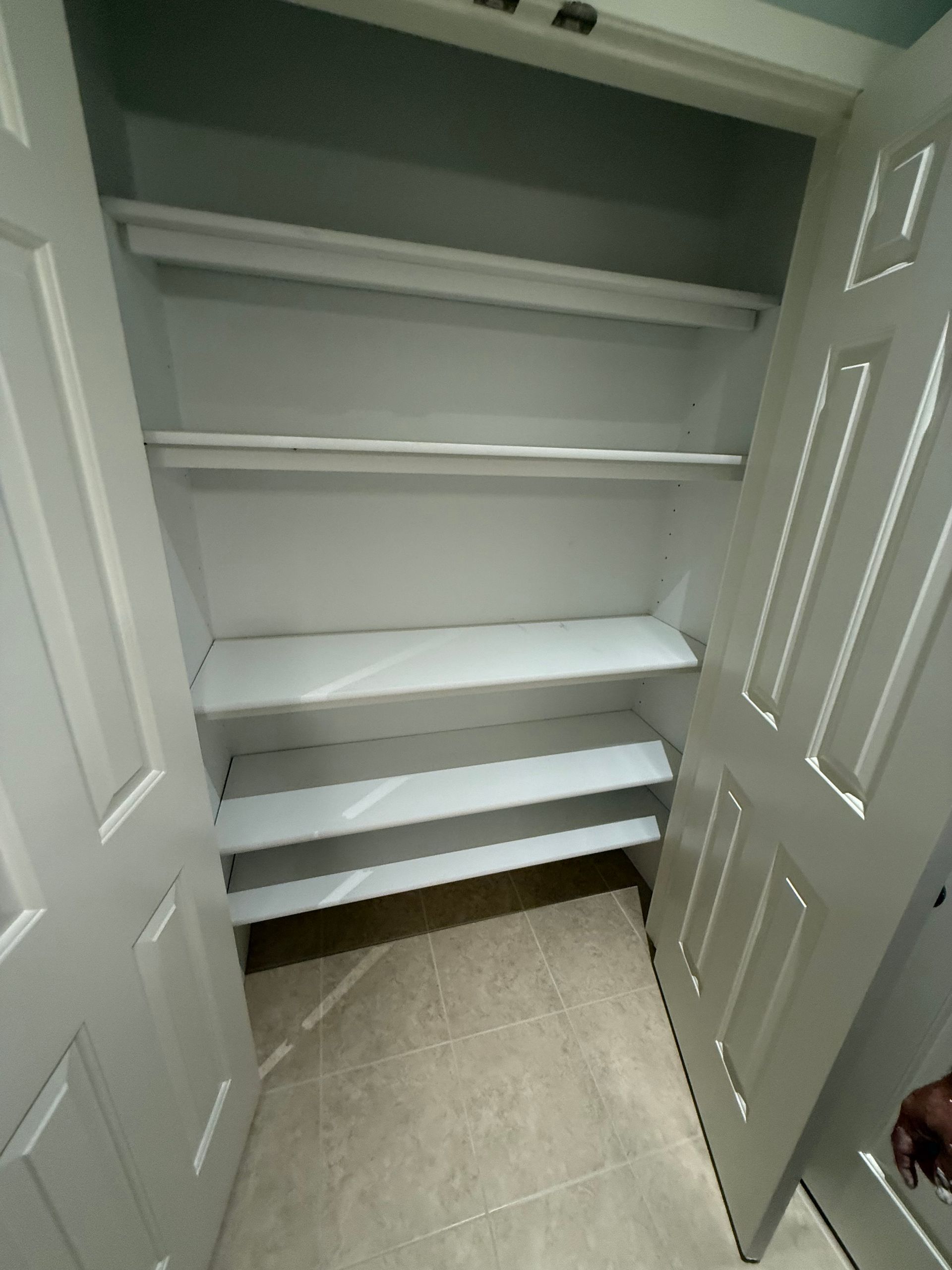 White closet with shelves and rods, open doors, and beige tile floor.