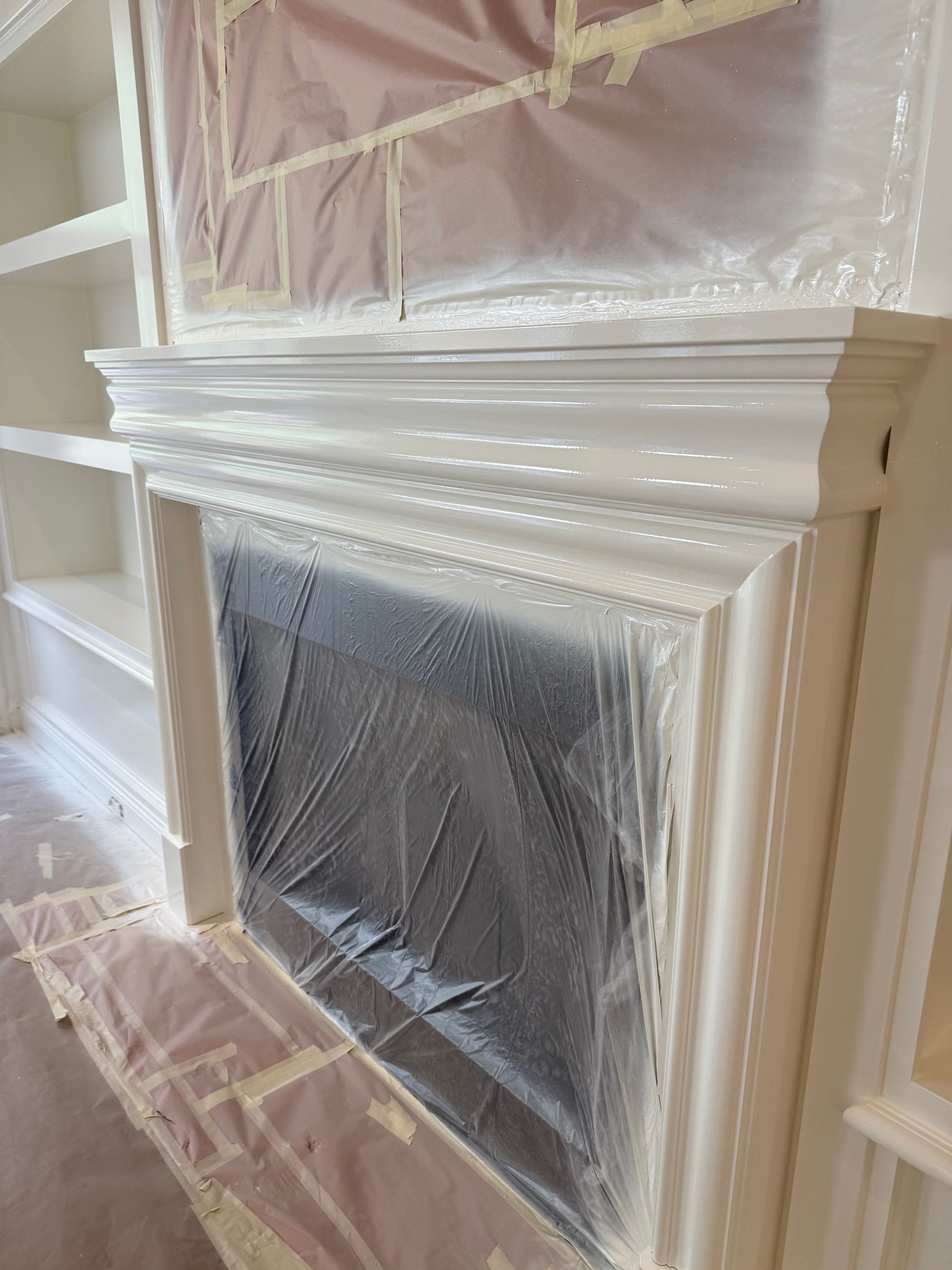 Fireplace mantel freshly painted white, plastic and tape protecting the fireplace and surrounding area.