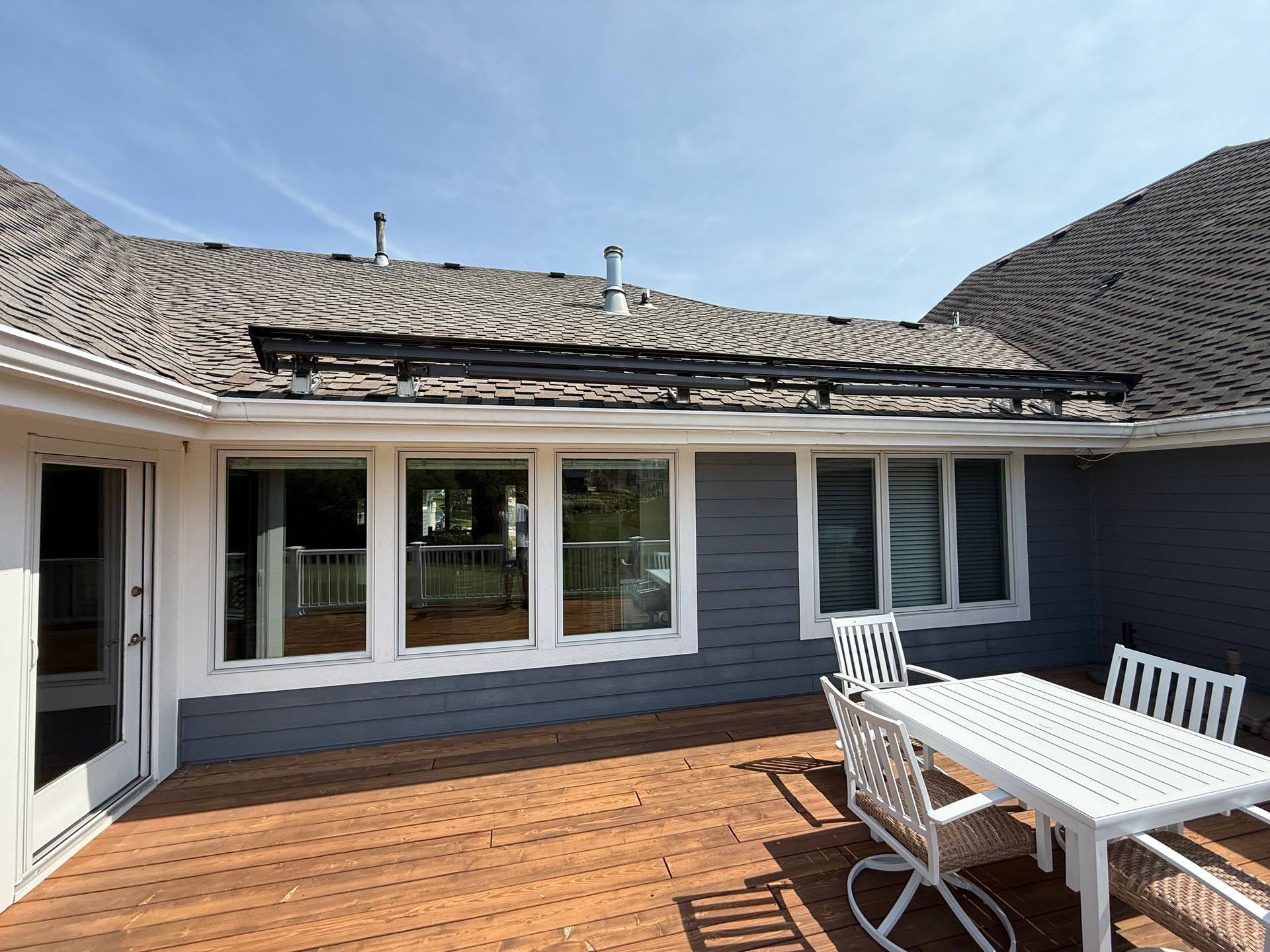 Wooden deck with a white table and chairs next to a gray house with windows and solar panels on the roof.