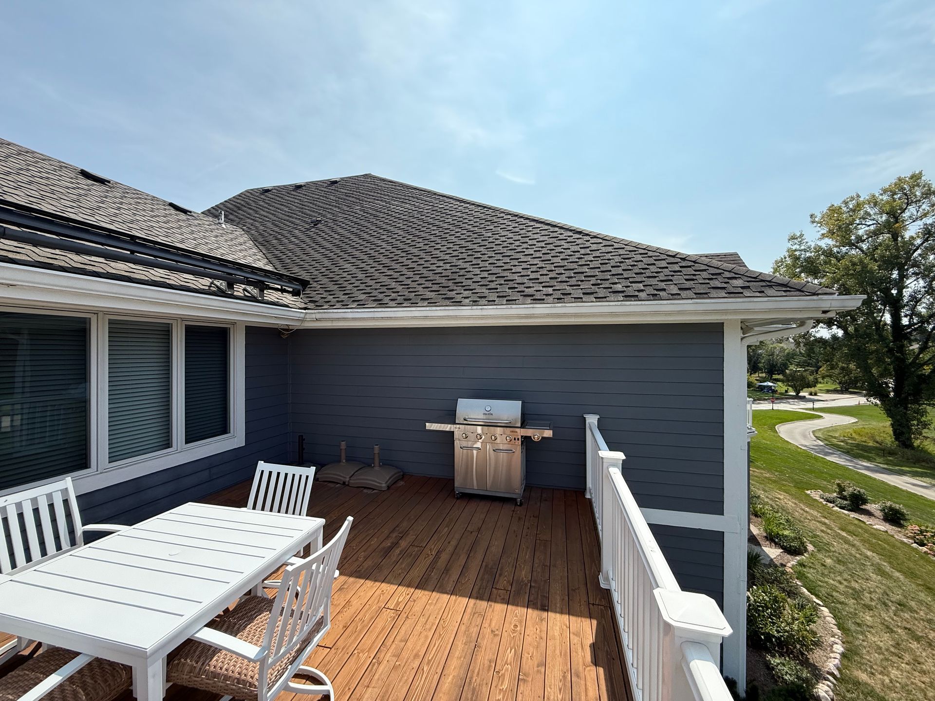 Wooden deck with outdoor dining set and grill next to a house with gray siding.