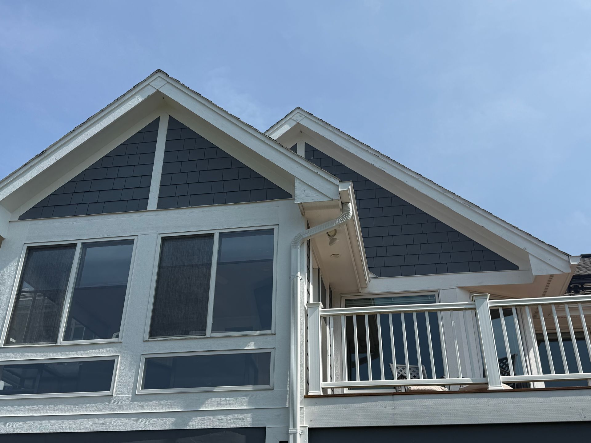 House exterior with dark blue roof, white trim, windows, and balcony against a blue sky.