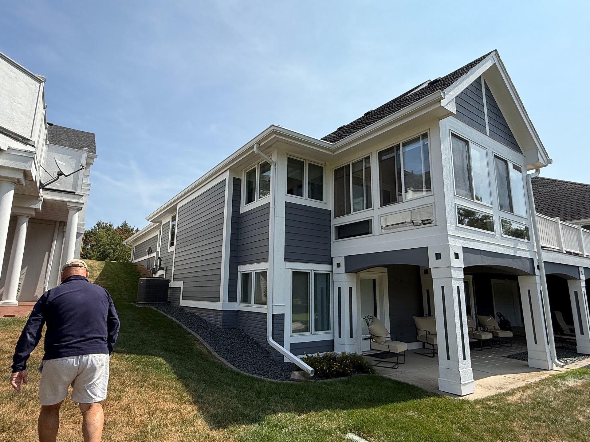 Man walks uphill toward a two-story house with blue and white siding, next to a similar building.