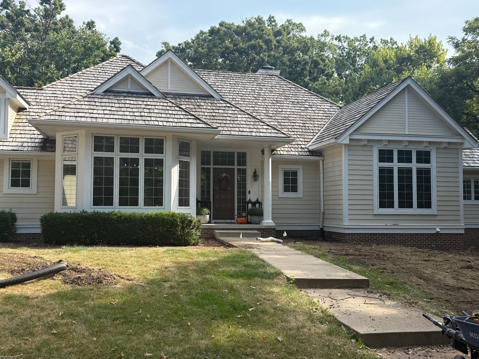 Tan house with wood shingle roof, large windows, and walkway through a grassy yard.