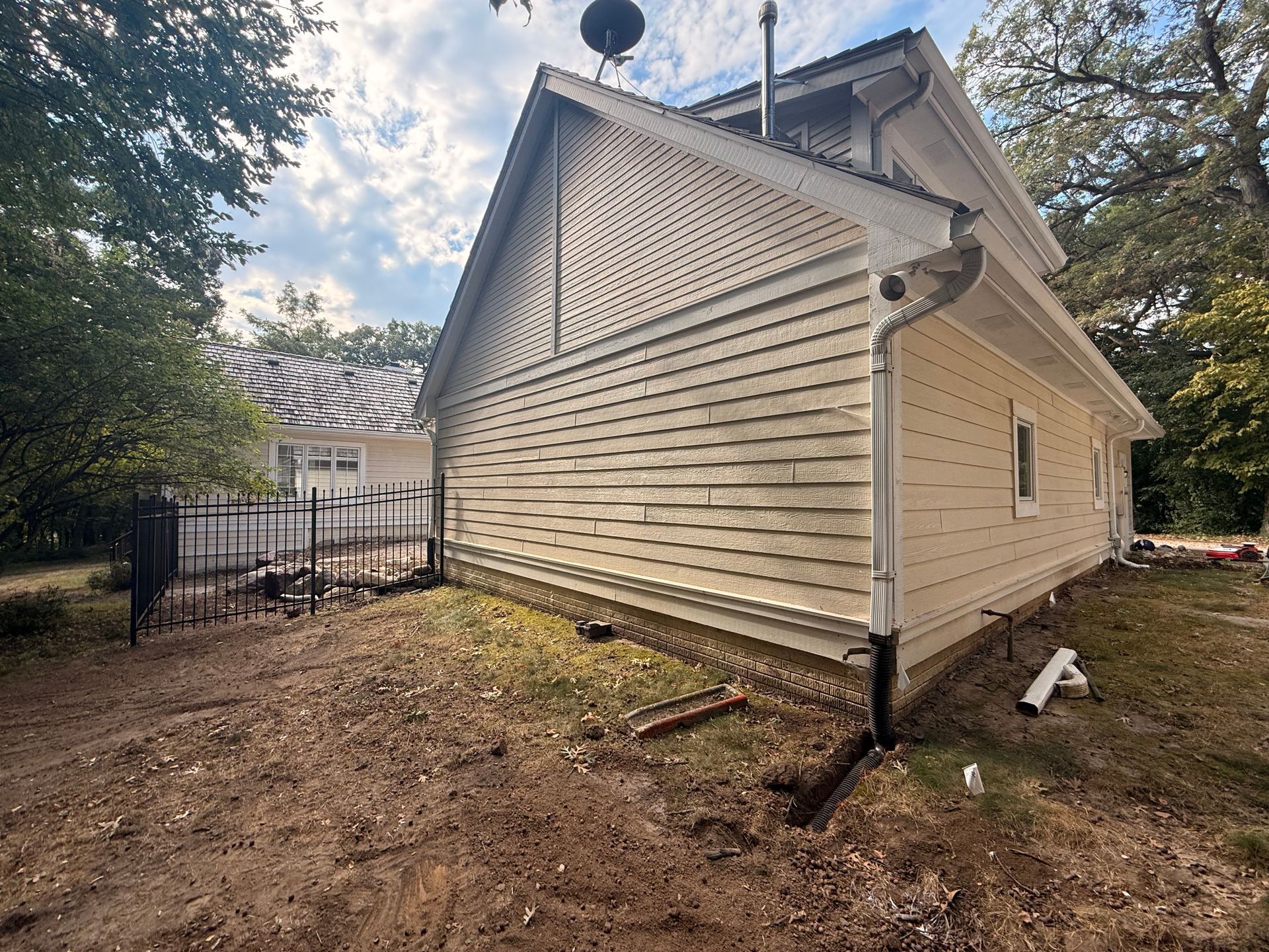 Side view of a two-story house with light yellow siding and a black fence in the yard.