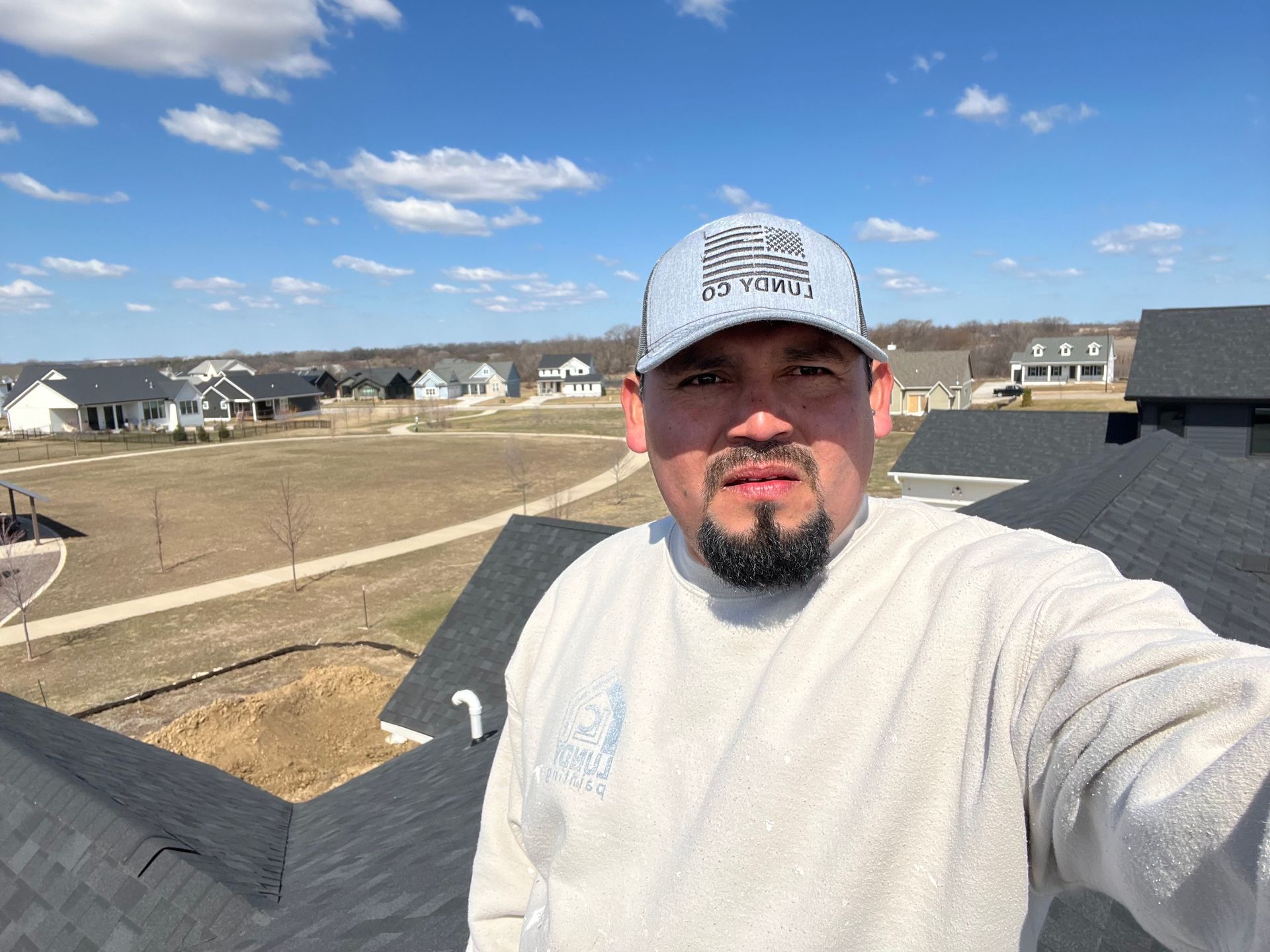 Man in cap and sweatshirt on a rooftop, with houses and blue sky in background.