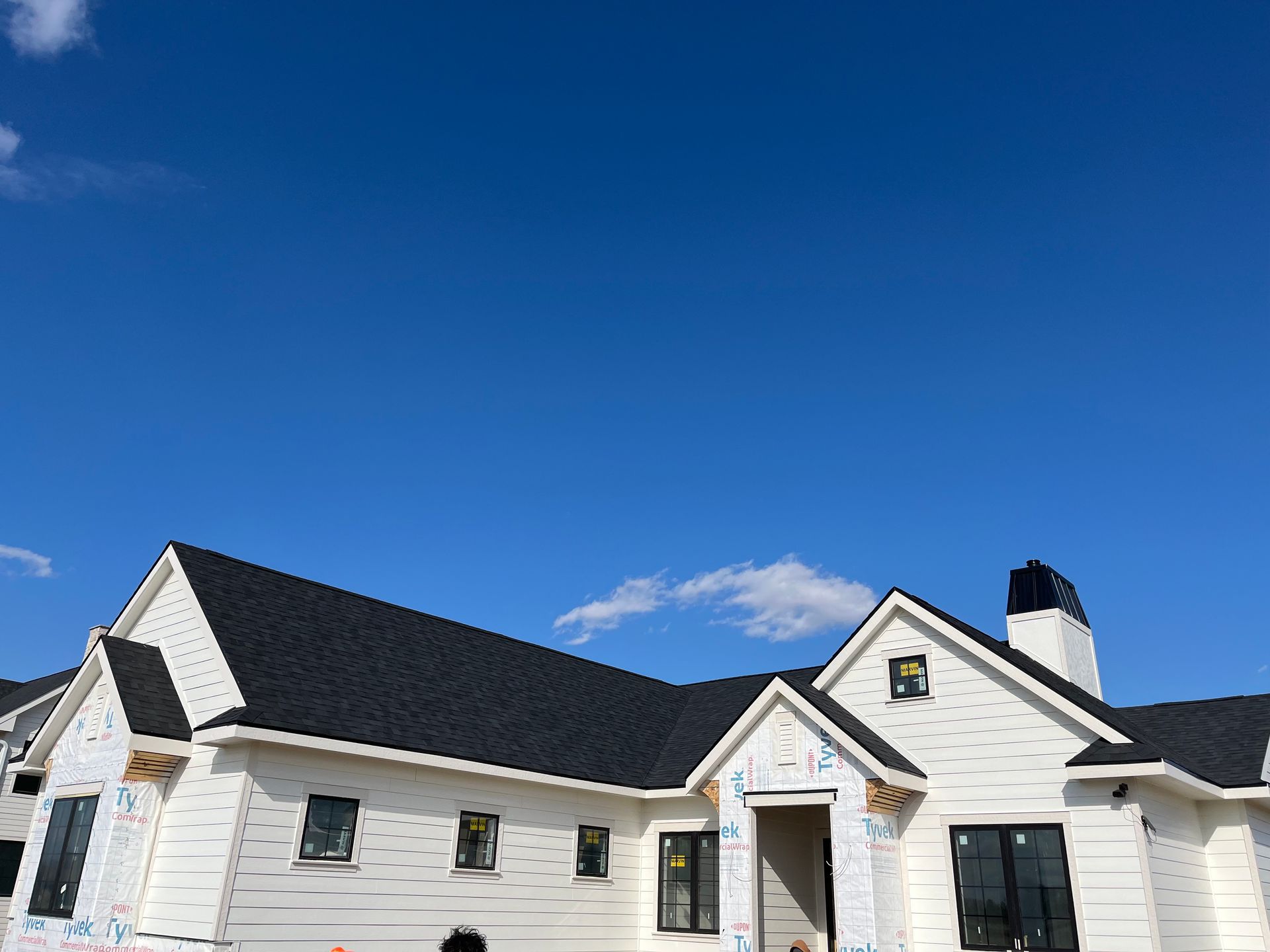 White house under construction, black roof against a bright blue sky.