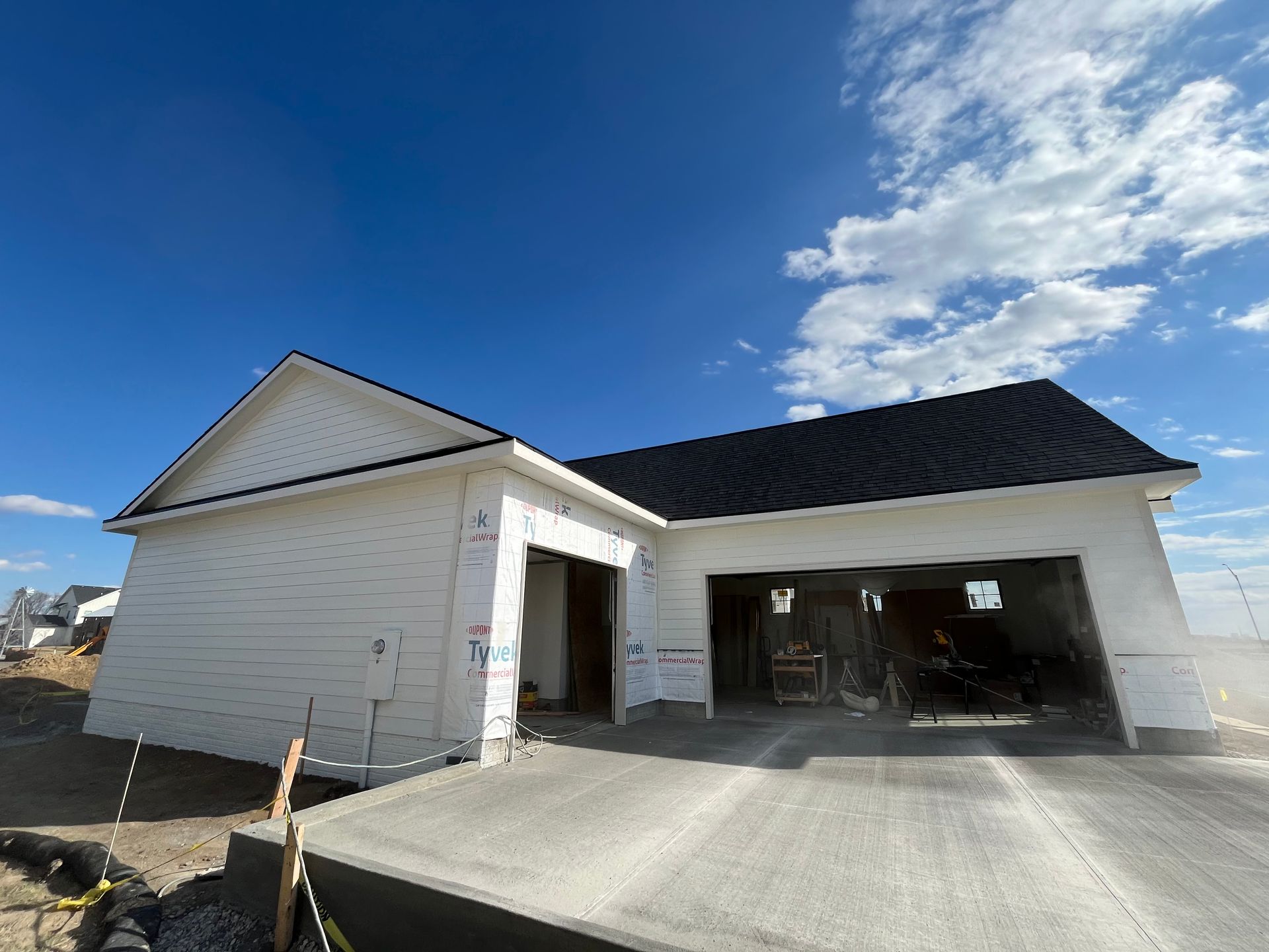 New house under construction with white siding, black roof, and open garage under a blue sky.