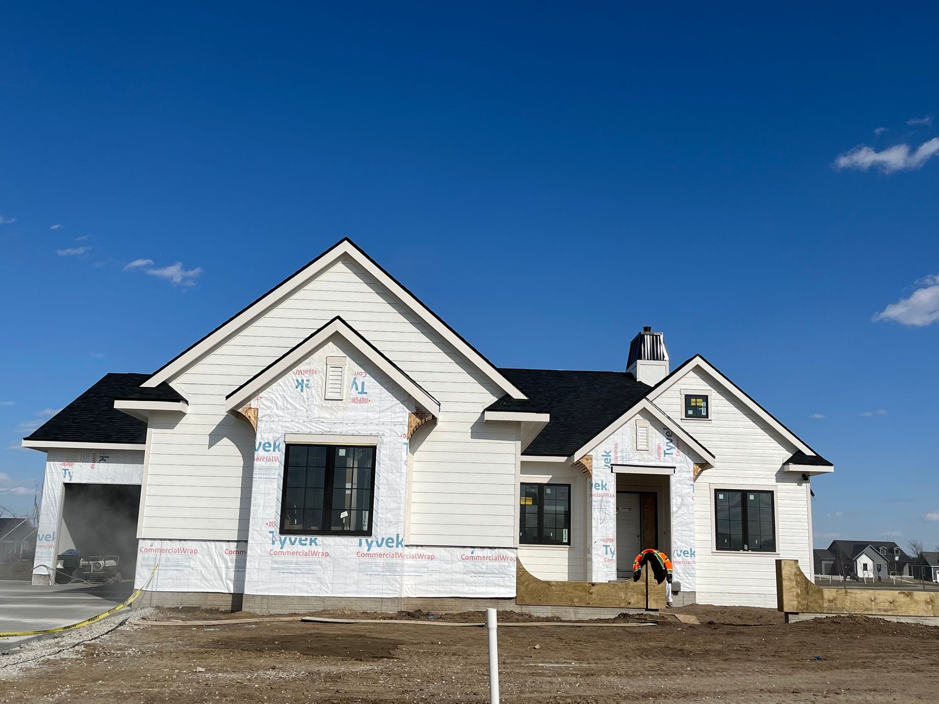 New house under construction with white siding, black roof, and clear blue sky.