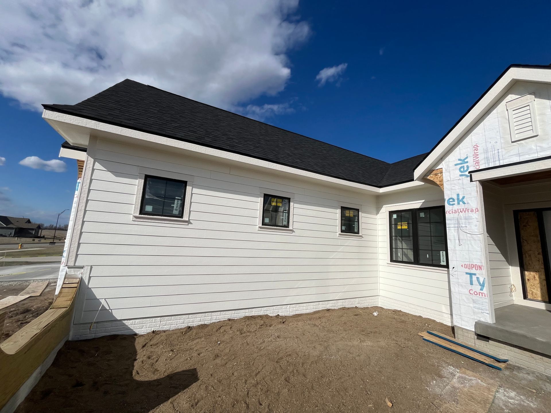 White-sided house under construction with black windows and roof against a blue sky.
