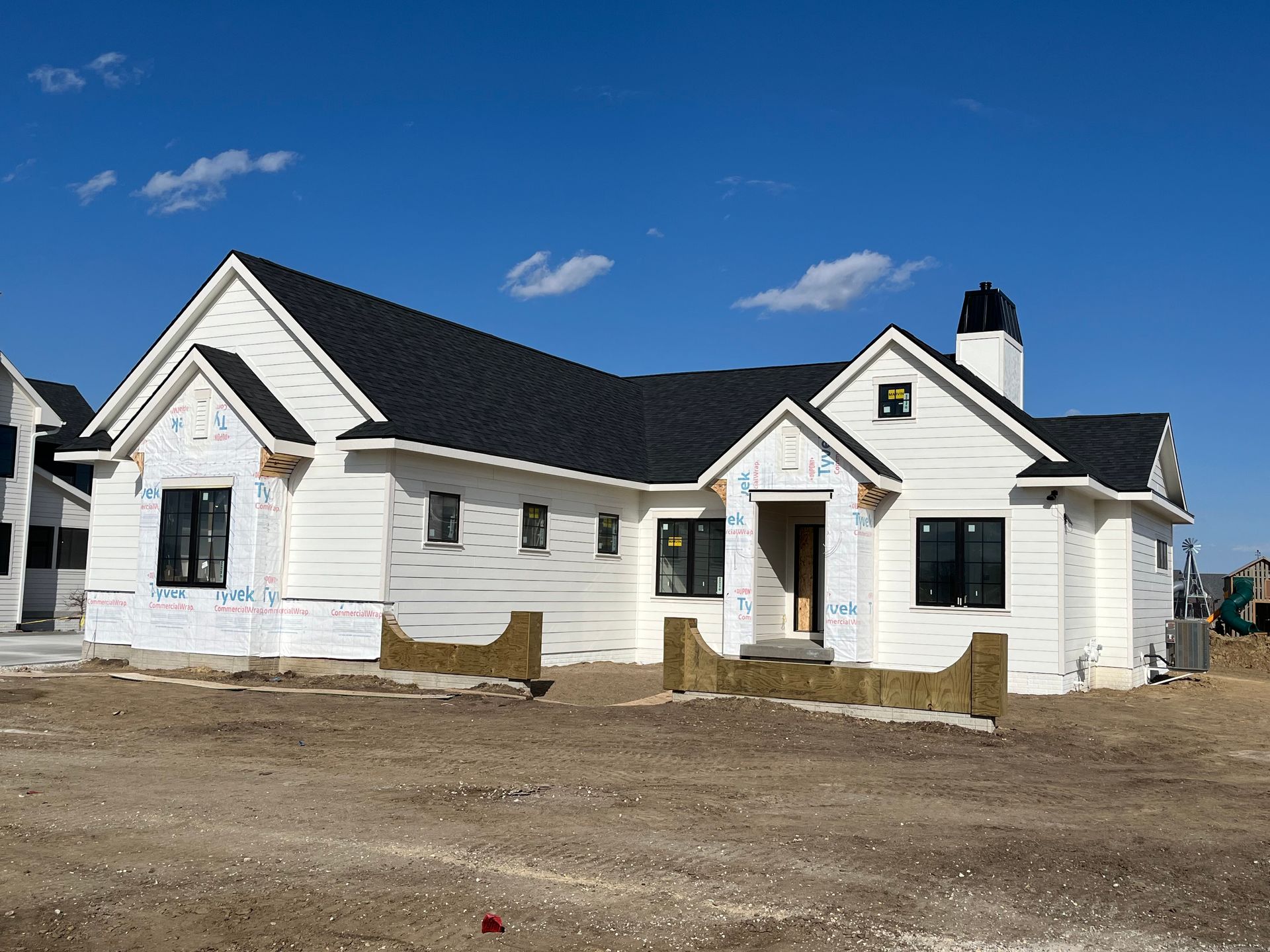 White house under construction with black roof and chimney against blue sky.