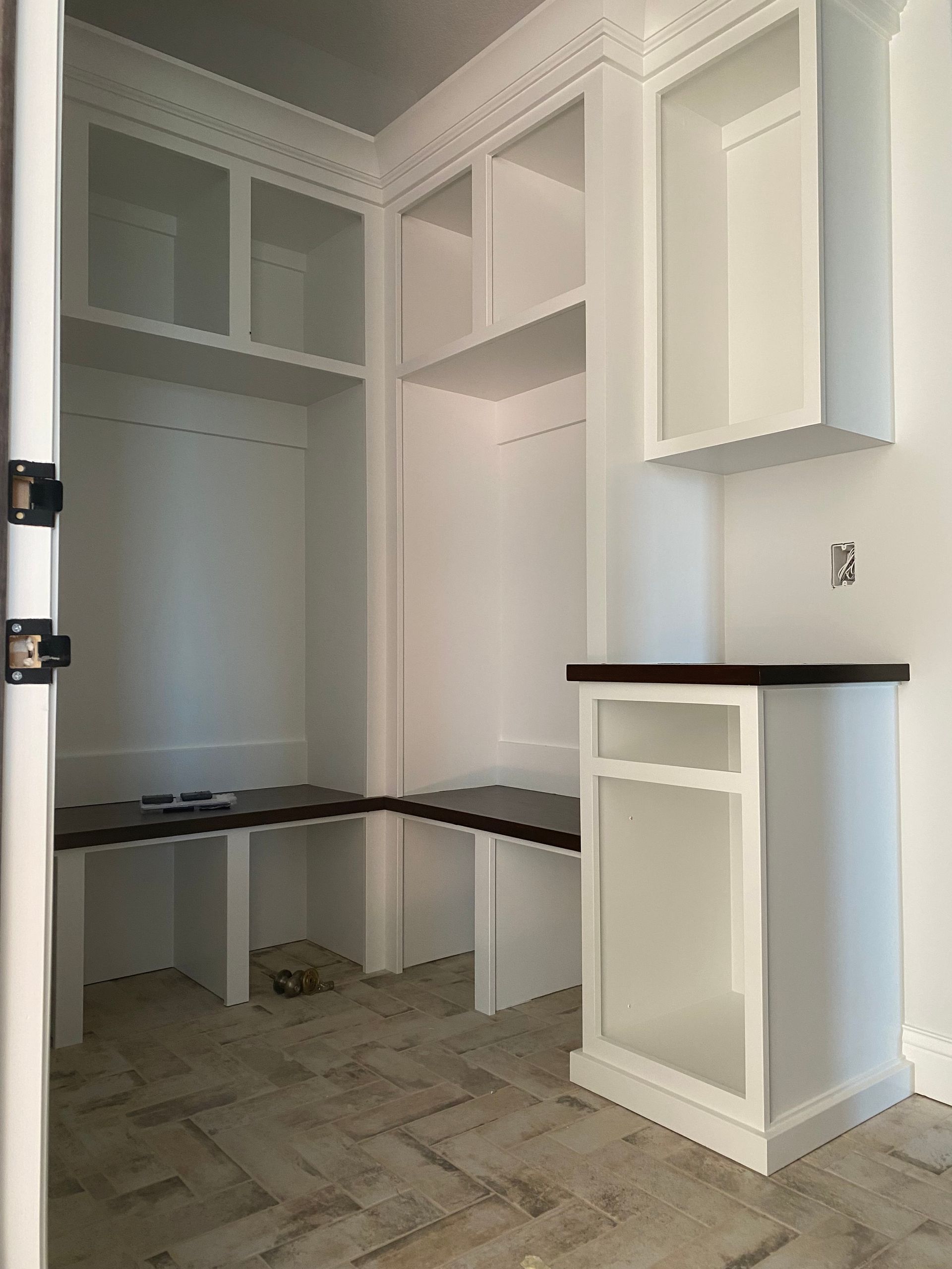 White built-in storage unit with shelves and dark wood countertops in an empty room, herringbone floor.