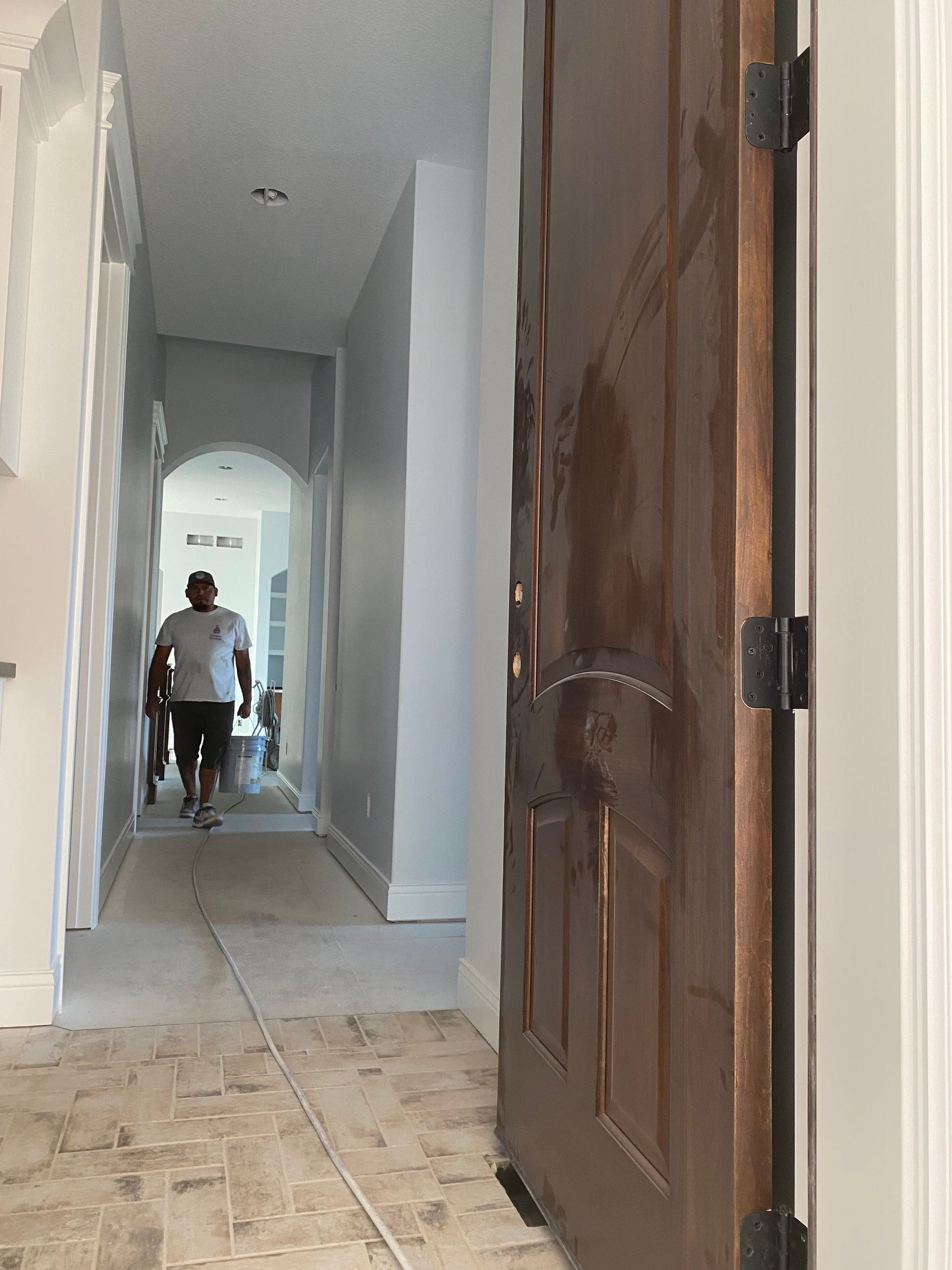 A man walks down a hallway towards a doorway. A dark brown door is in the foreground.