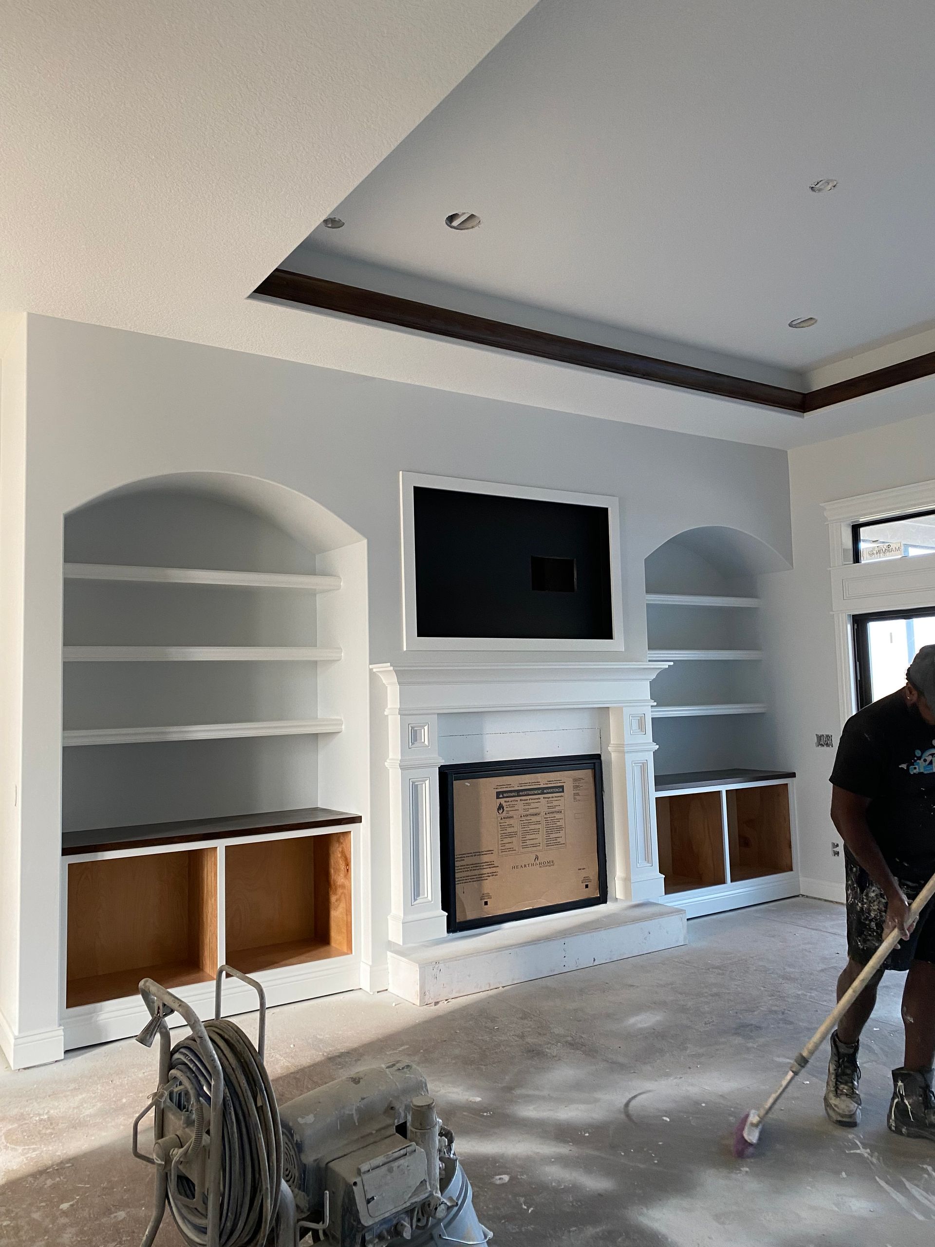 Interior with freshly painted white walls, built-in shelving, fireplace, and a worker painting the floor.
