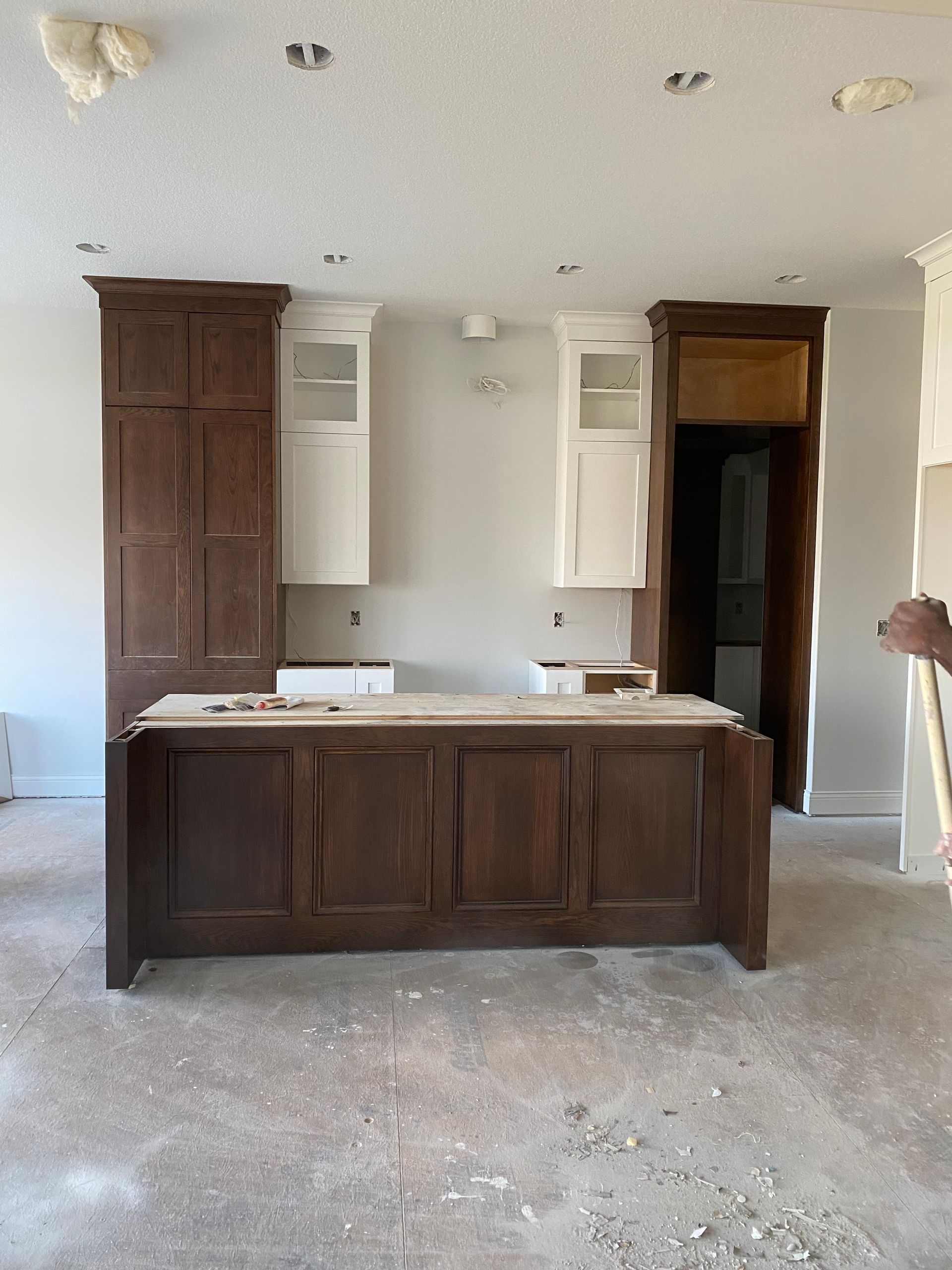 Kitchen cabinets and island in progress, unfinished. Brown and white cabinets against light walls, open doorway.