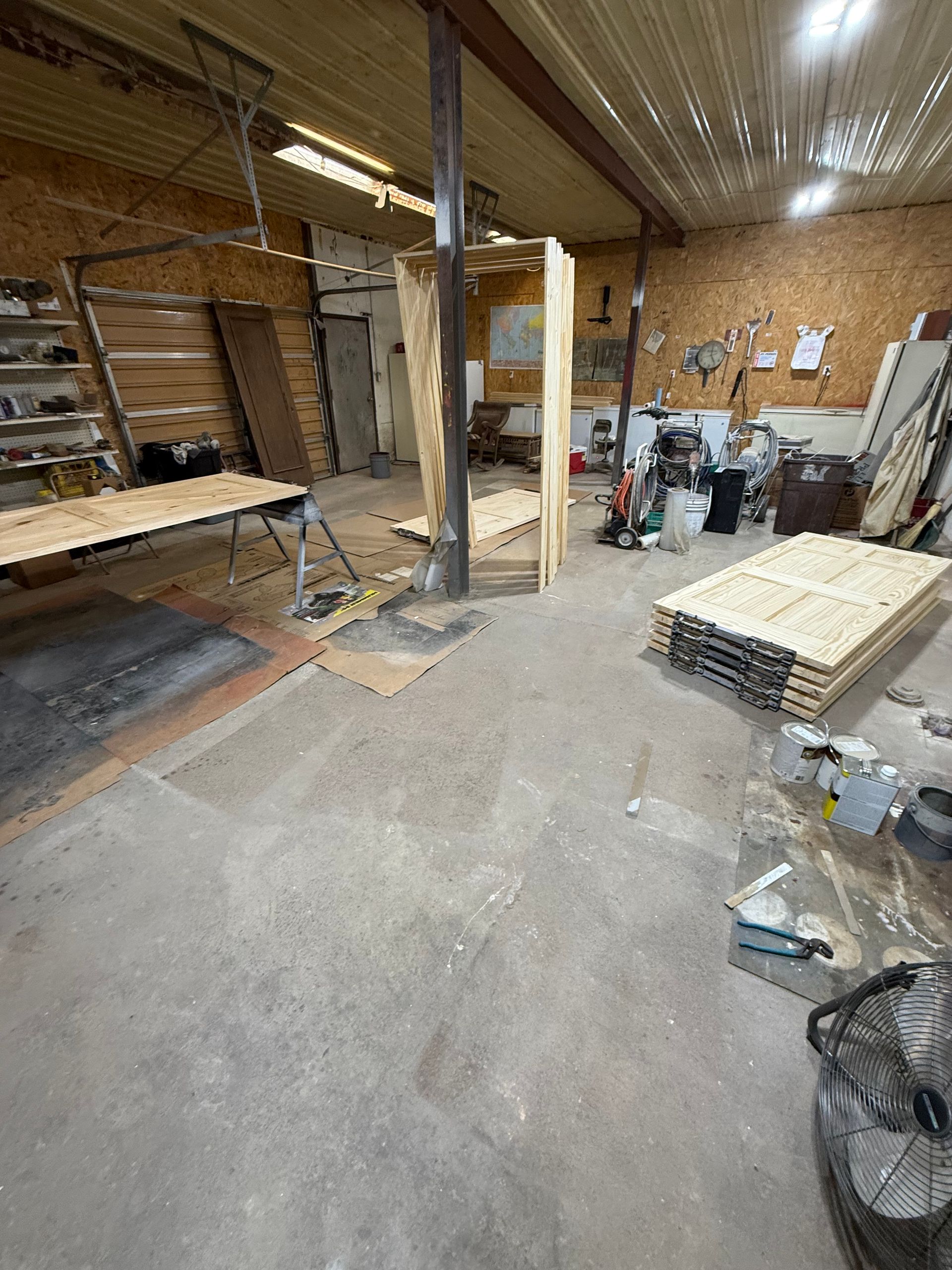Workshop interior with wooden construction underway; cluttered with tools, materials, and a large fan.