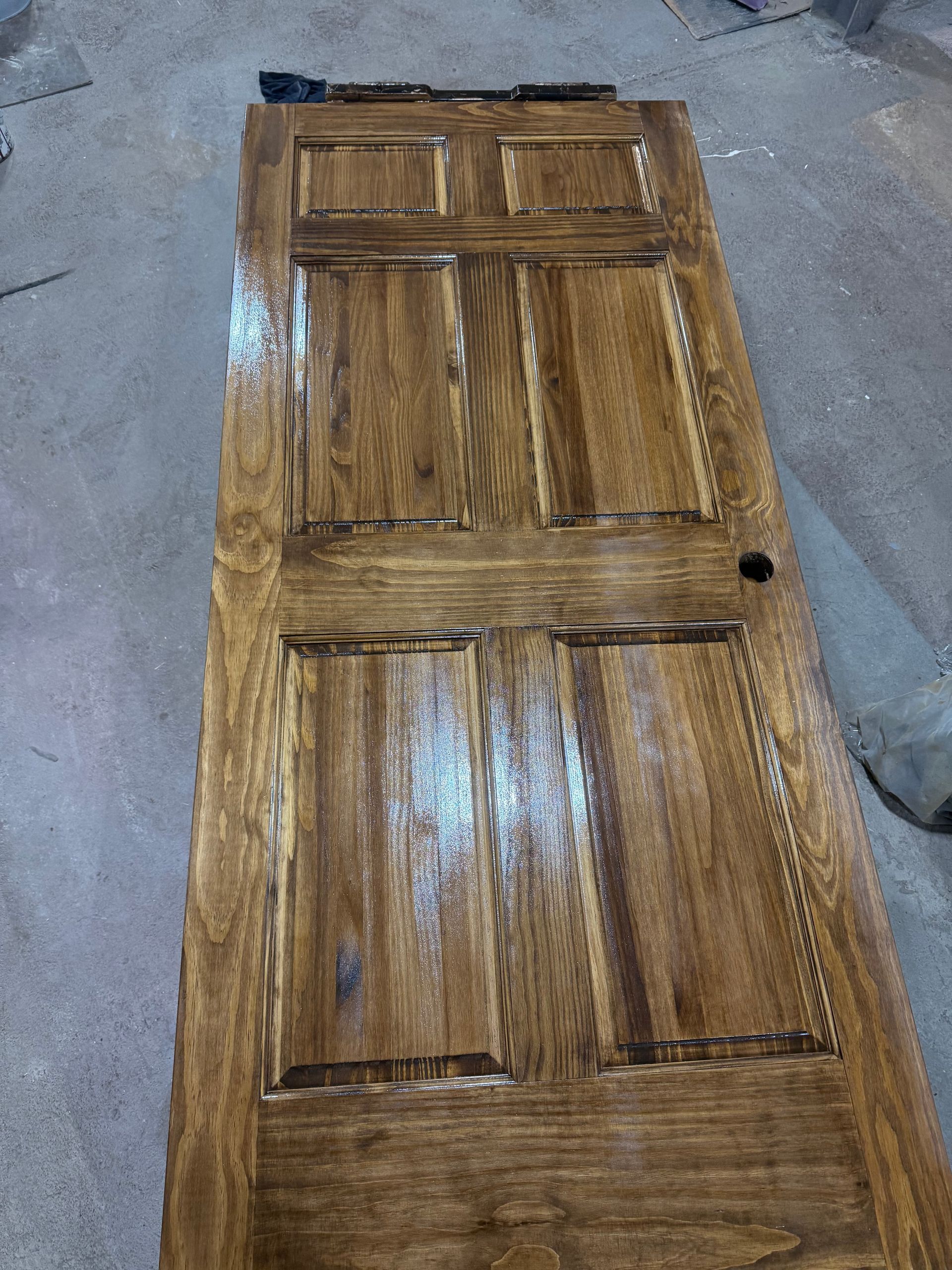 Wooden door with a stained finish lying on a concrete floor.