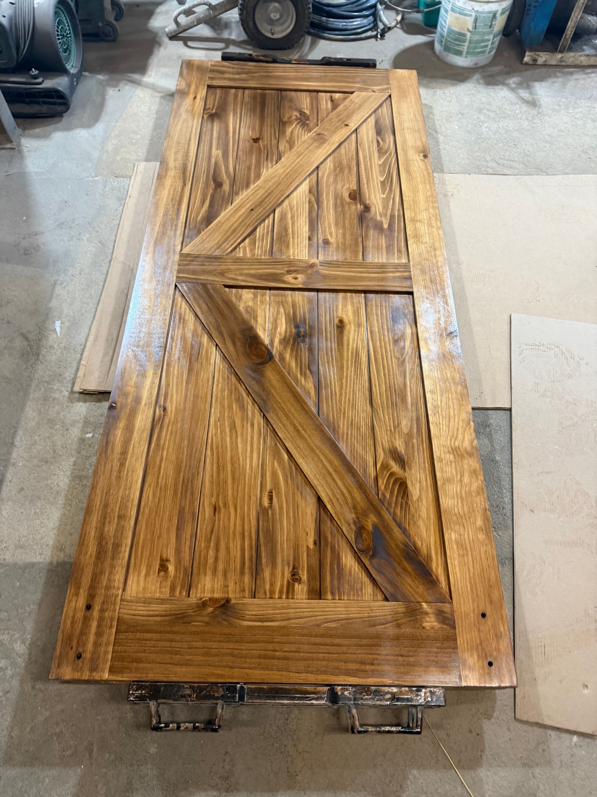 Wooden barn door stained brown, with diagonal support beams, lying on a work surface.