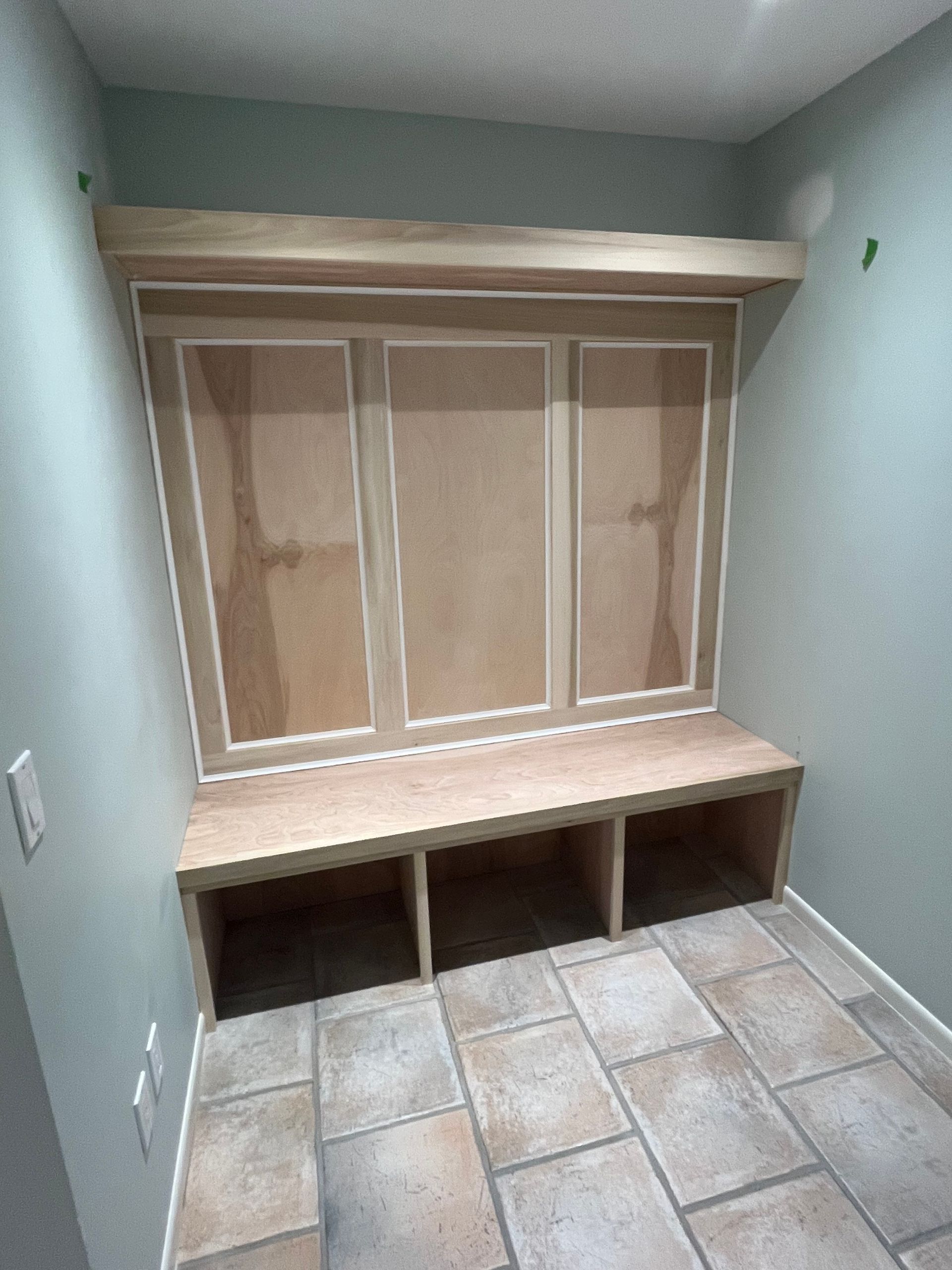 Built-in entryway storage with bench and overhead shelf in room with tiled floor and green walls.