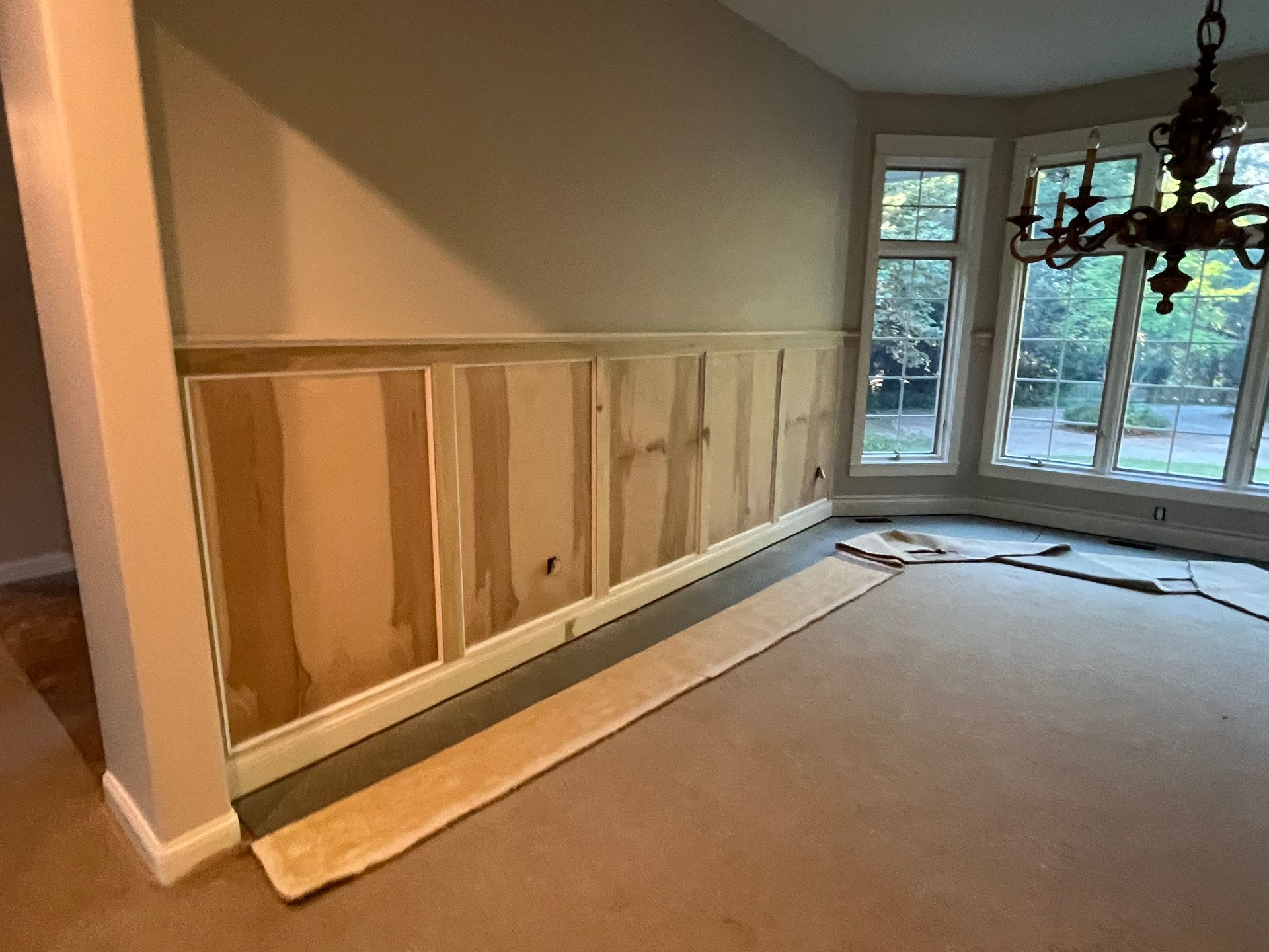 Dining room with partially installed wood paneling on the wall; carpeted floor and windows.