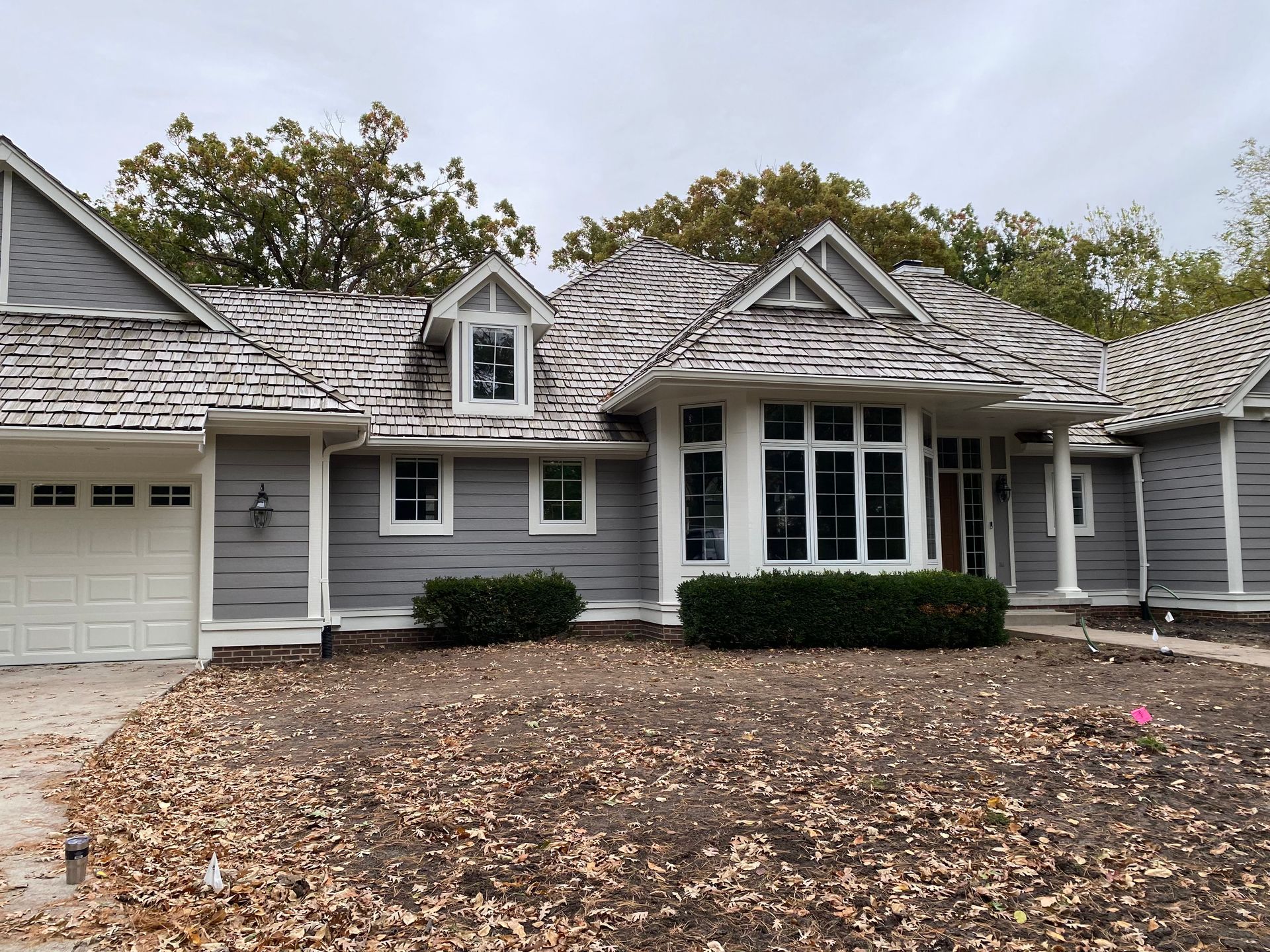 Gray house with cedar shake roof, white trim, and a yard covered in leaves.