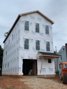 New construction multi-story building with Tyvek wrap, windows installed, and an open garage bay.