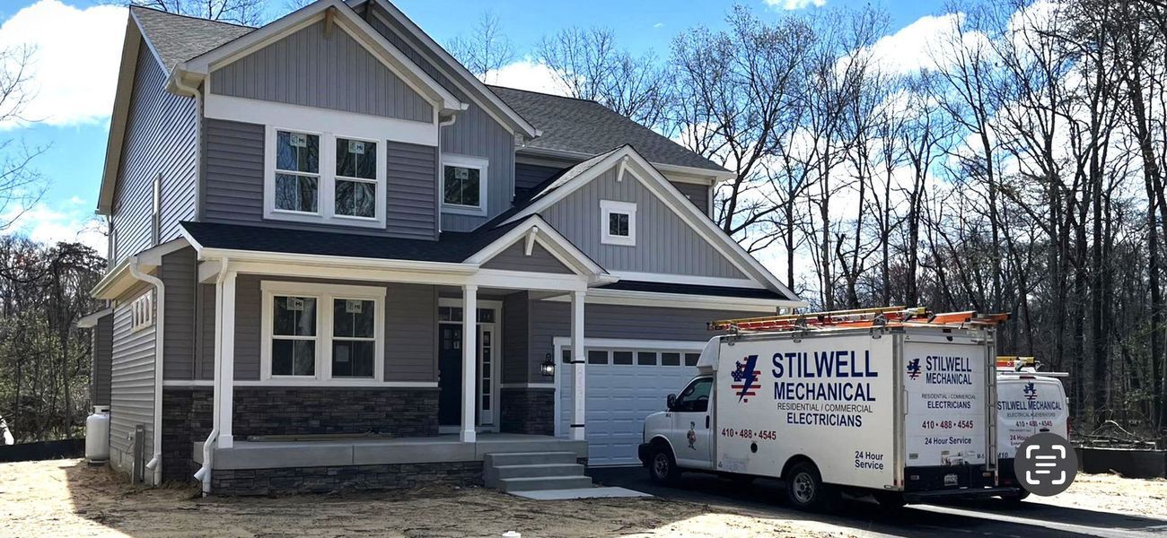 Two-story house with gray siding, a white garage door, and a Stillwell Mechanical service van in front.