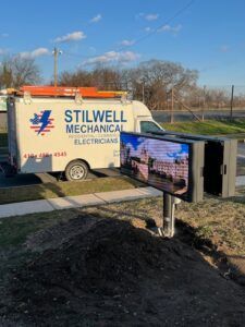 A Stilwell Mechanical van parked near an illuminated outdoor digital display.