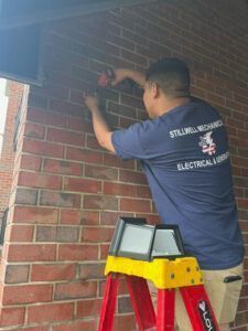 Man in blue shirt on ladder working on brick wall.