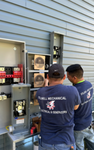 Two men in matching shirts installing electrical equipment on a building's exterior.