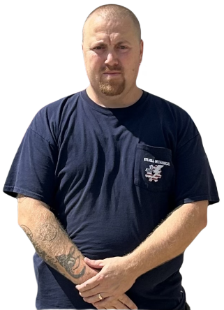Man with goatee wearing a blue t-shirt with arm tattoo, arms crossed, standing.