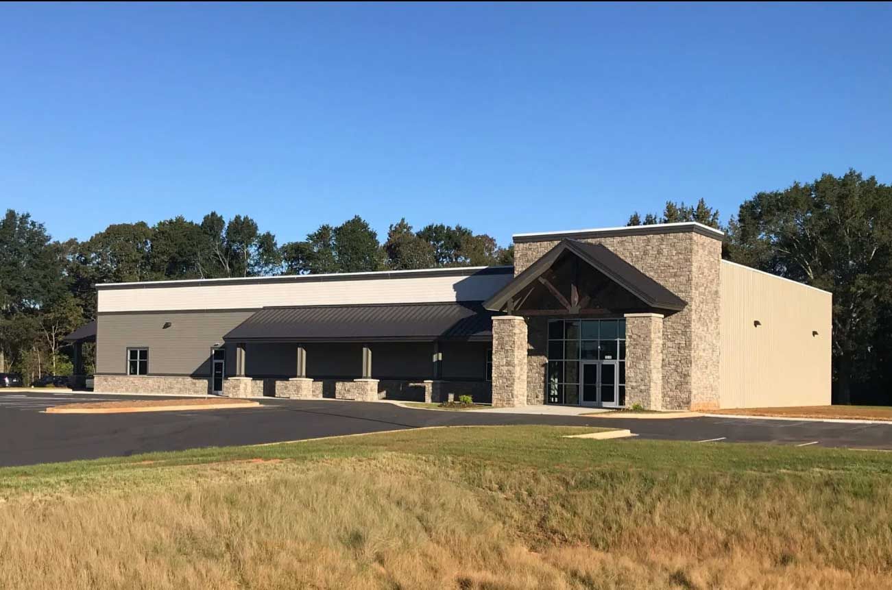 A modern, single-story commercial building with stone facade, dark metal roof, and an entrance under a peaked porch.