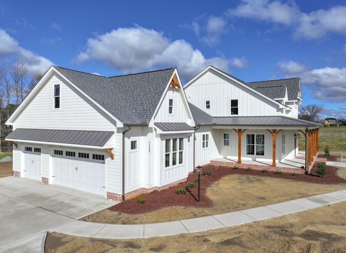 A large white house with a gray roof is sitting on top of a dirt field.