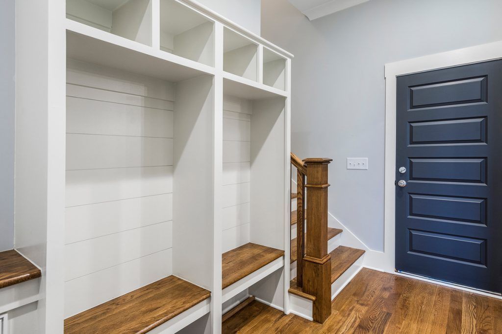 A mud room with a blue door and stairs in a house.