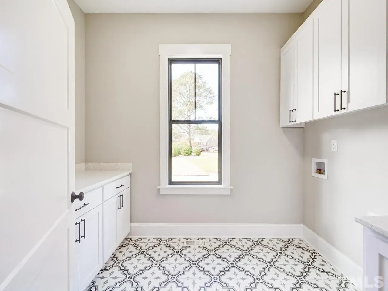 A laundry room with white cabinets and a window.
