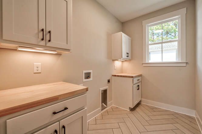 A laundry room with white cabinets and a window.
