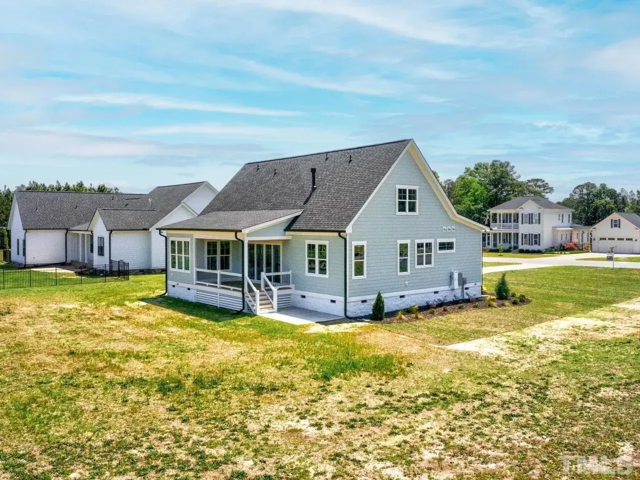 A white house with a porch is sitting on top of a lush green field.