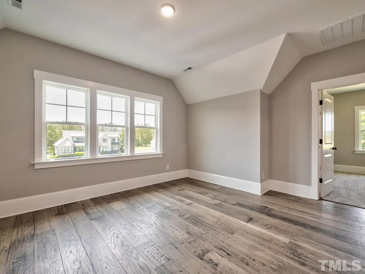 An empty room with hardwood floors and three windows.
