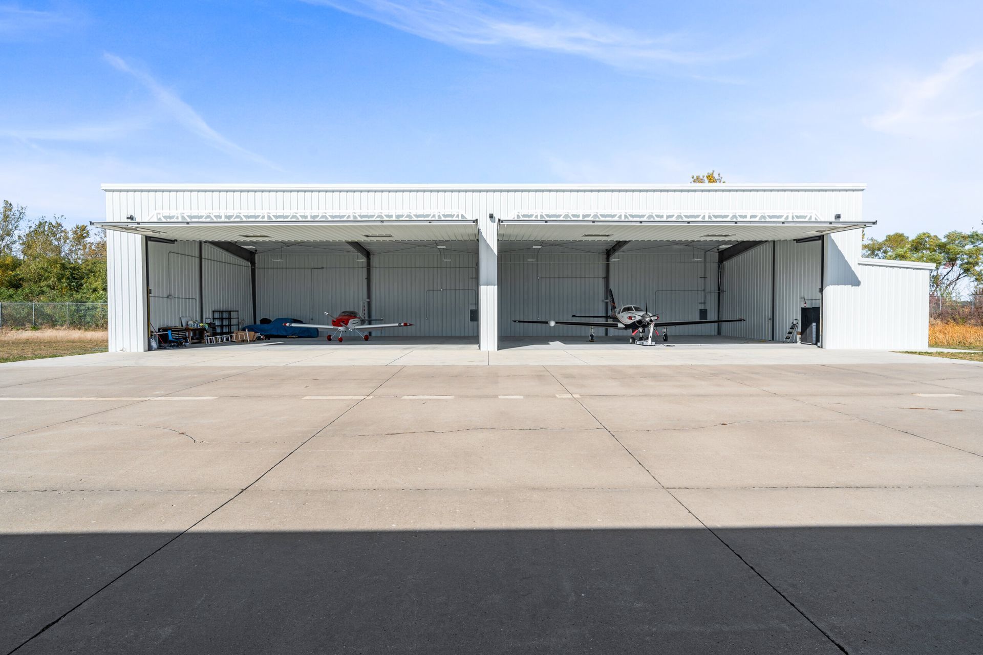 Two-bay airplane hangar with planes inside, on a paved airfield, under a blue sky.