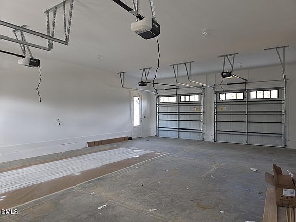 Empty garage with three overhead doors, three garage door openers, and a concrete floor.