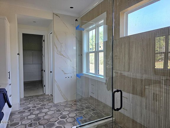 Bathroom with shower, window, hexagon tile floor, light-colored walls and door leading to a walk-in closet.